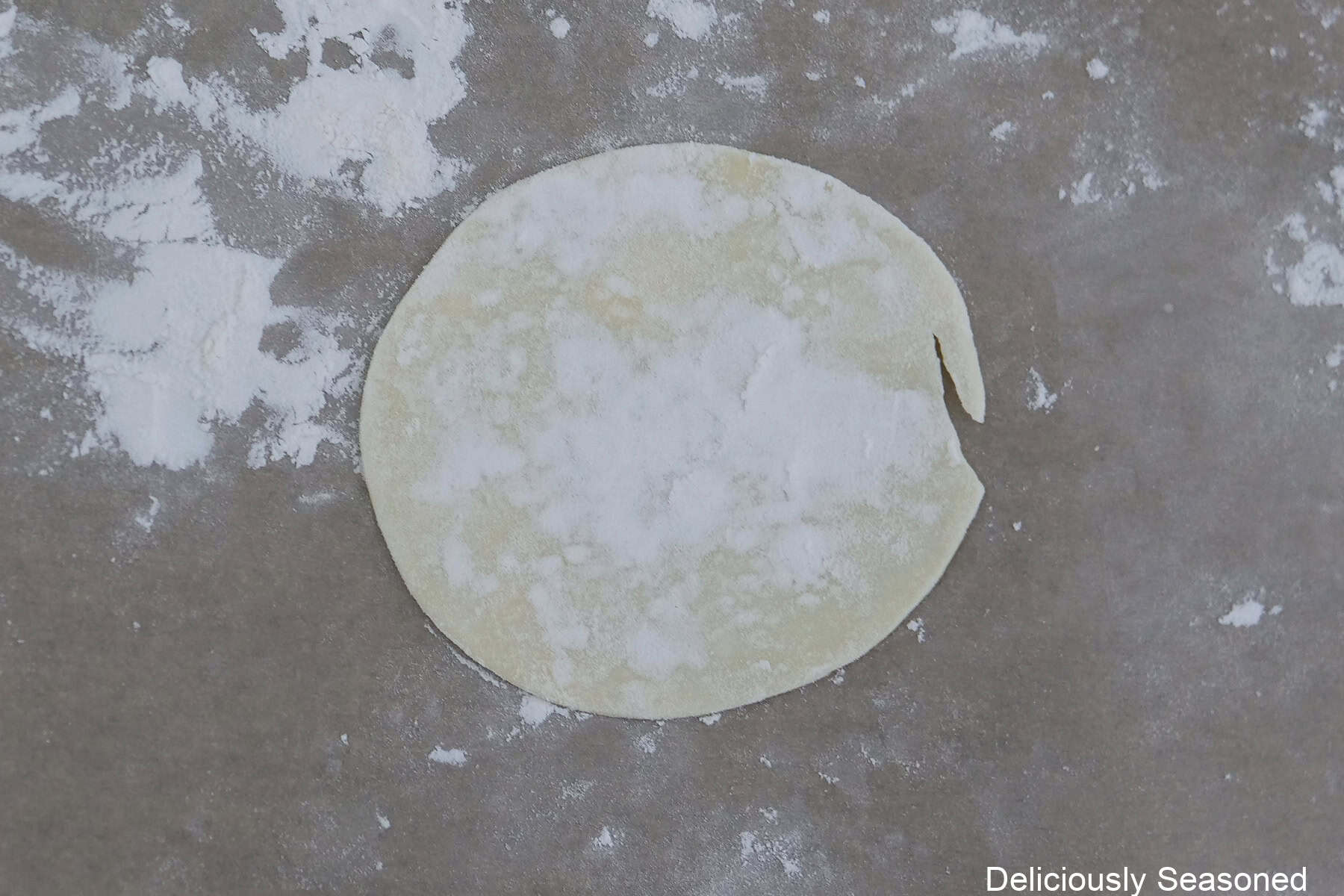 A counter top lightly floured with one empanada dough on it with a little flour on it.