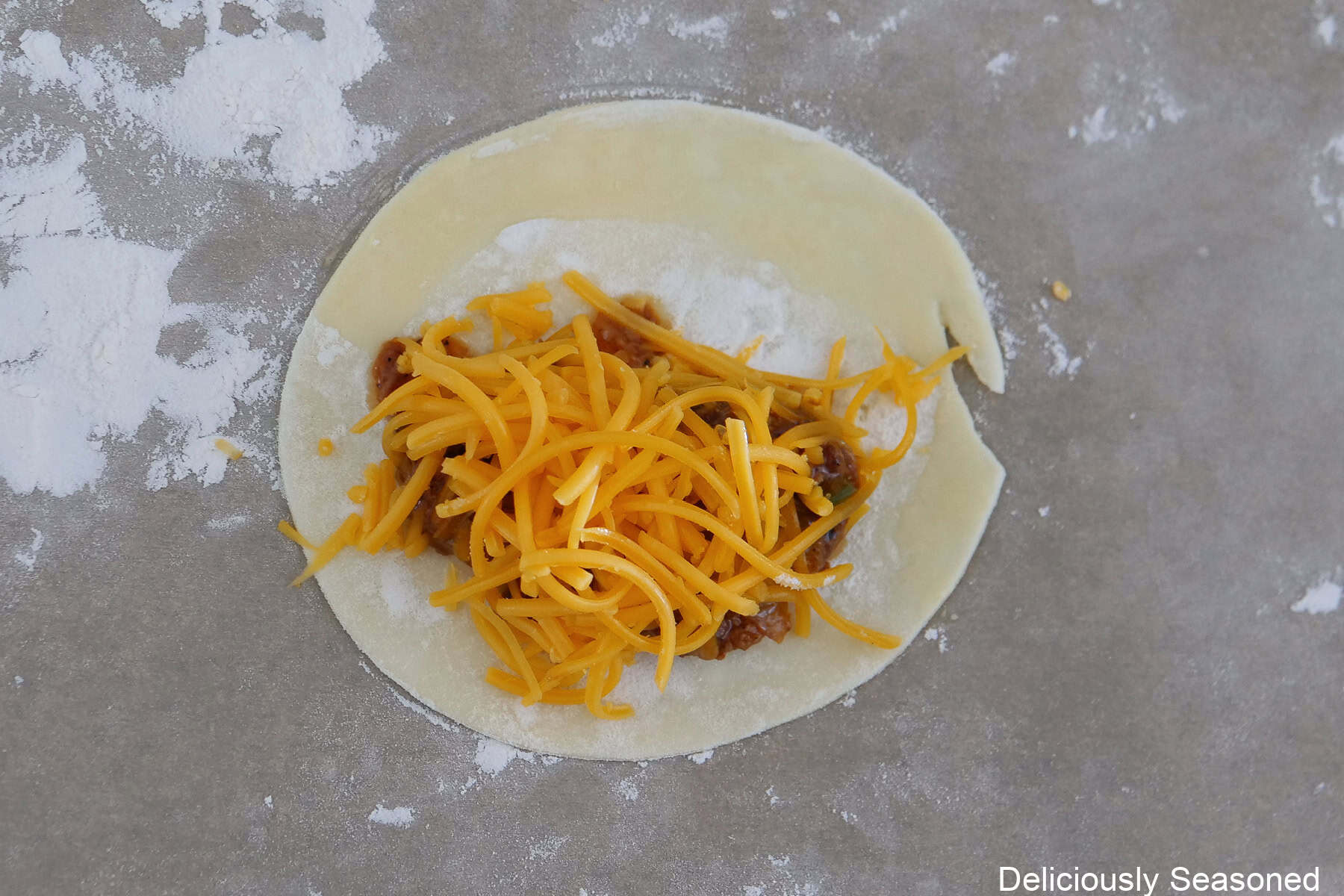 A lightly floured countertop with brisket and shredded cheese on empanada dough.