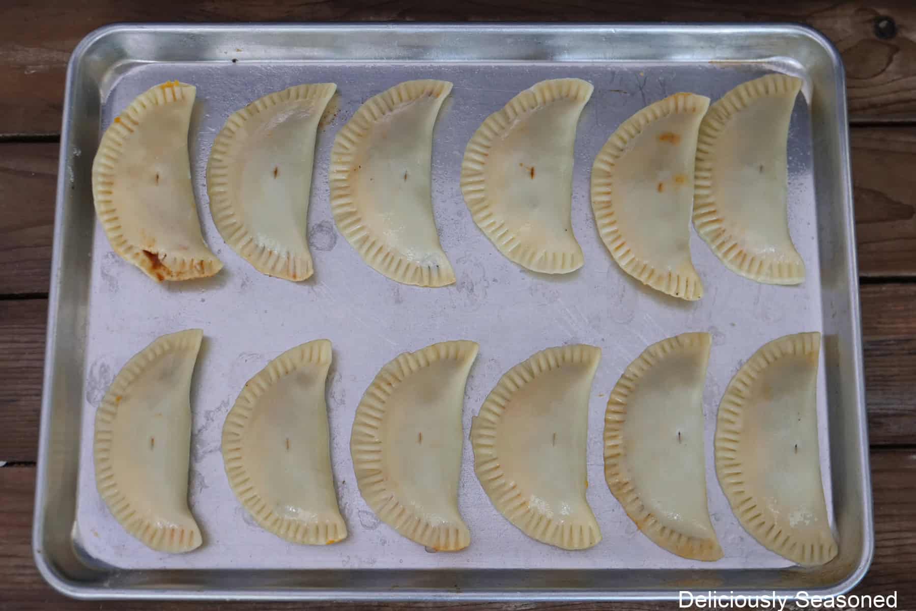 A silver baking sheet with twelve beef brisket empanadas placed on it after being filled before going into the oven.