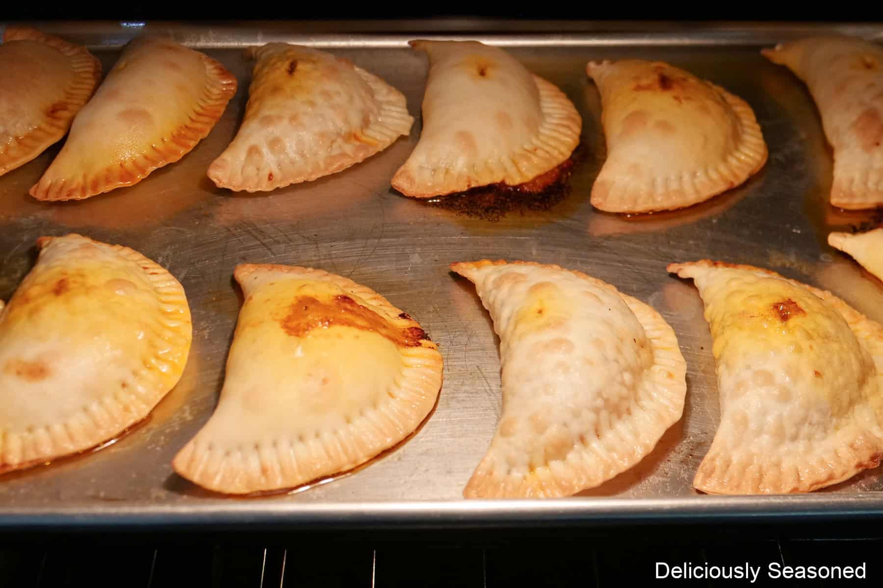 A baking sheet with twelve beef brisket empanadas on it baking in the oven.
