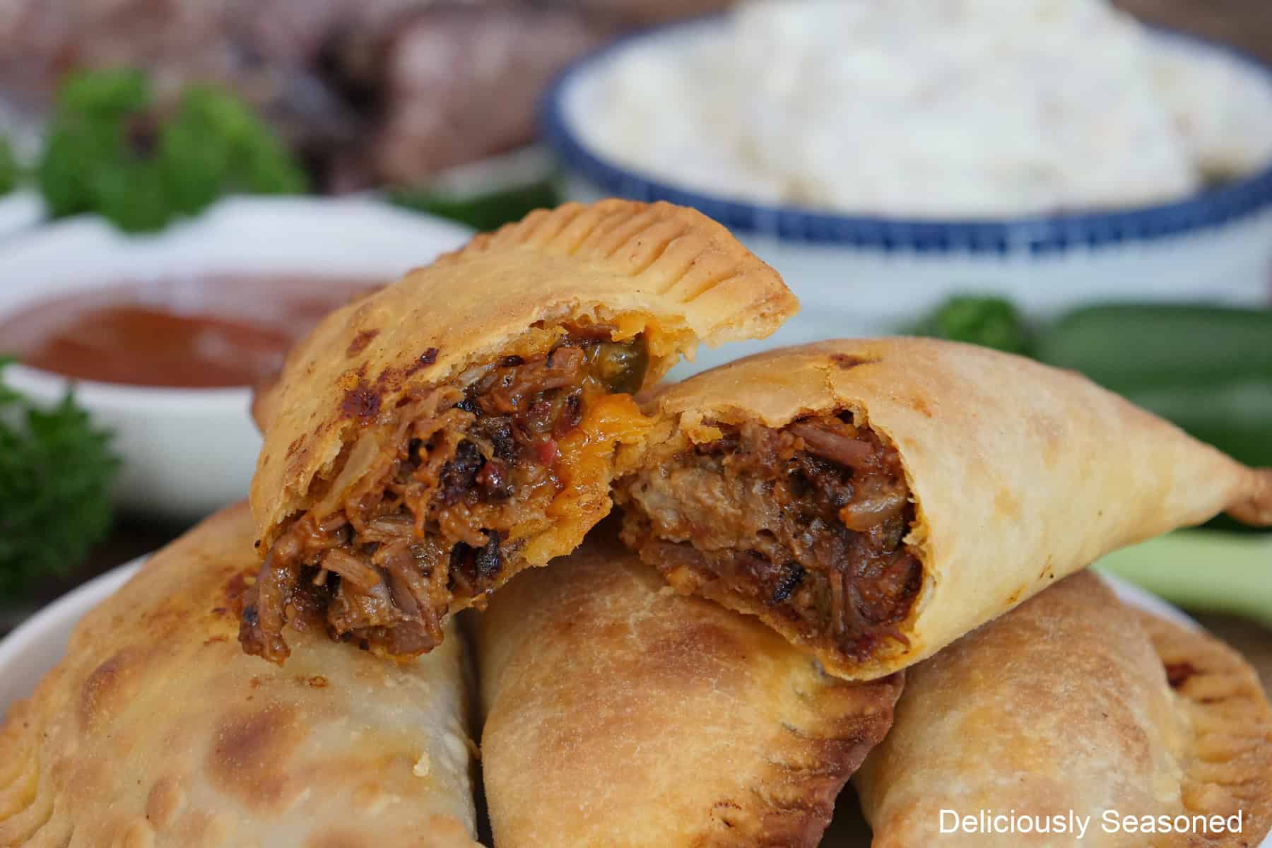 Five beef brisket empanadas on a plate with two of them with bites taken out showing the inside meaty ingredients.