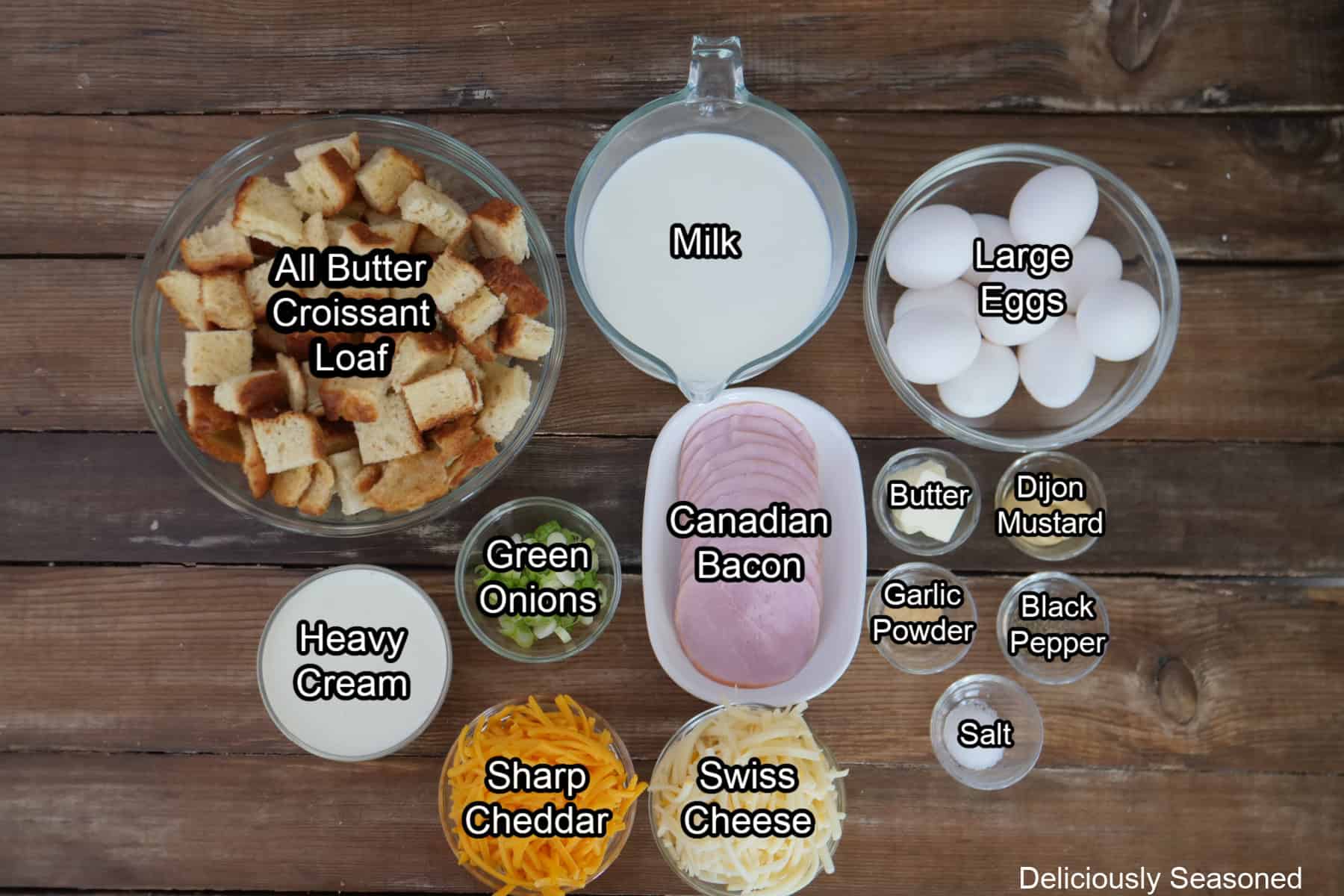 A wood surface with all the ingredients placed on it to make cheesy ham bread pudding.