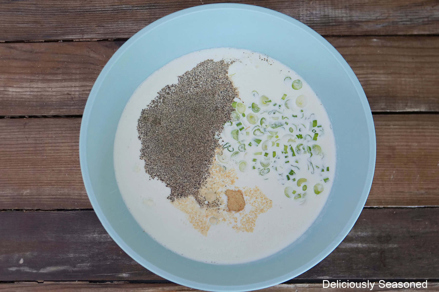 A wood surface with a blue bowl filled with the savory custard ingredients in it.