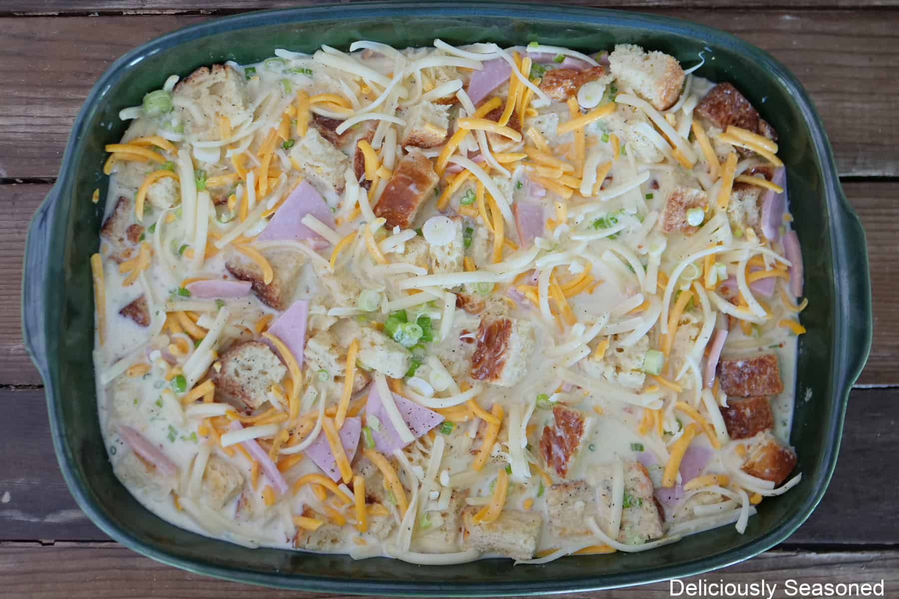 A 9 by 13 green baking dish filled with cheesy ham bread pudding before going in the oven to bake.