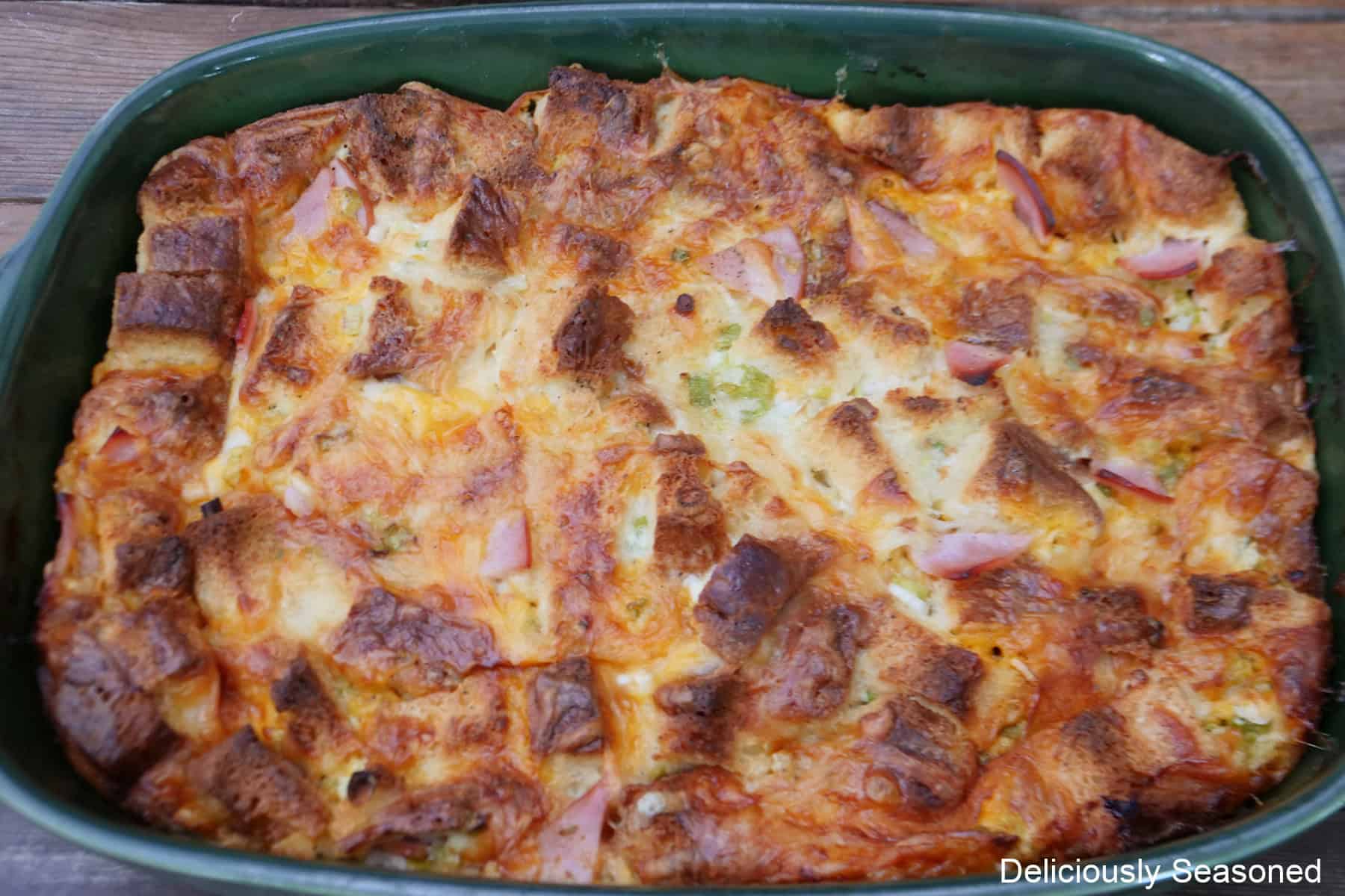 A baked cheesy ham bread pudding in a green 9 by 13 baking dish.