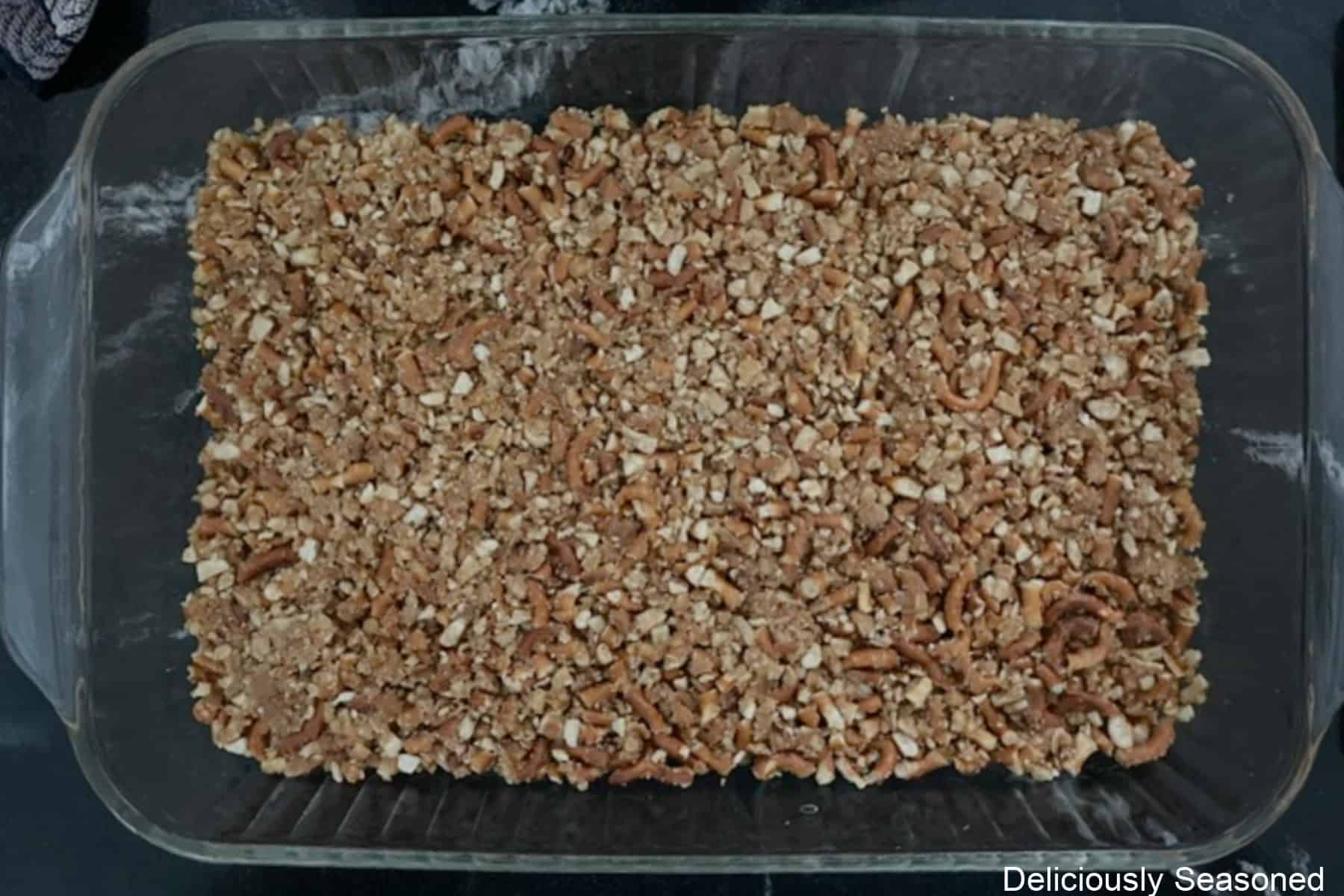 A black countertop with a glass 9 by 13 baking dish with a pretzel crust in it.