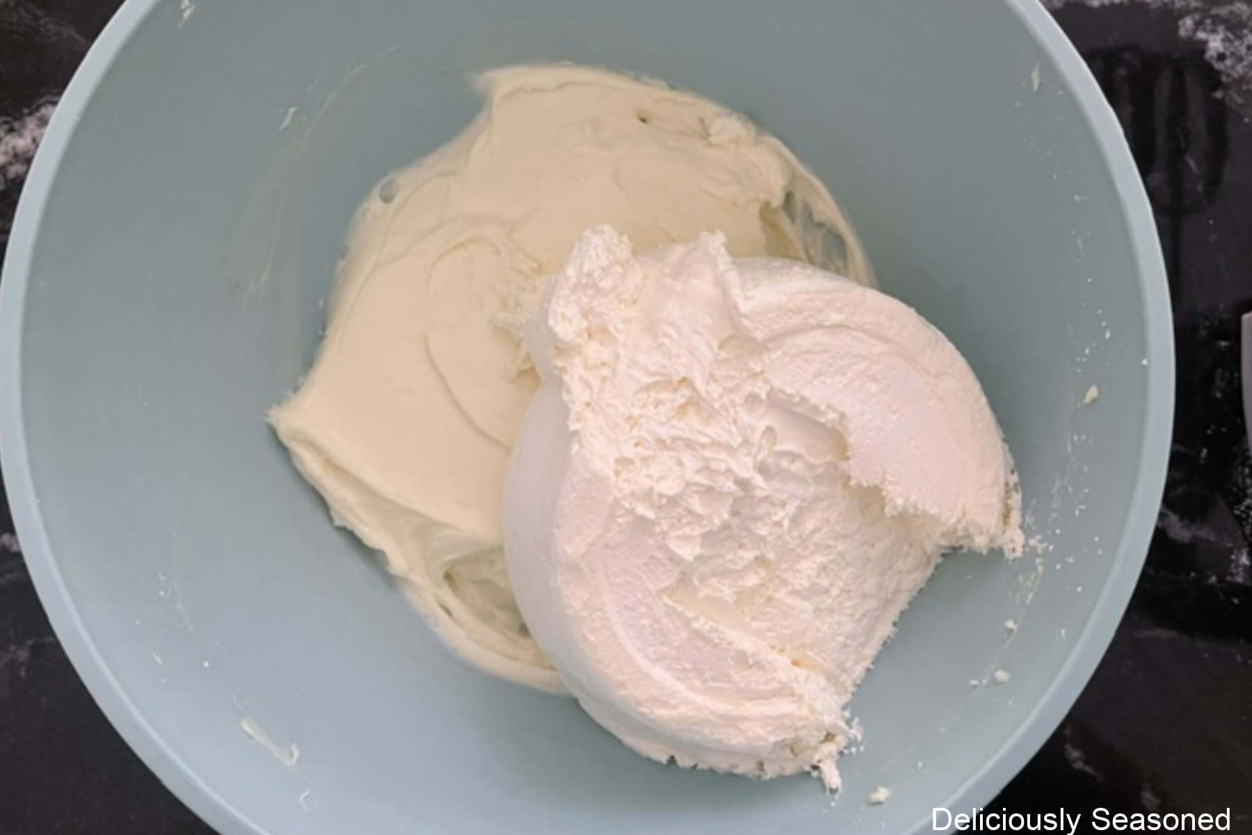 A light blue bowl with a cream cheese mixture in it and the cool whip about to be folded in.
