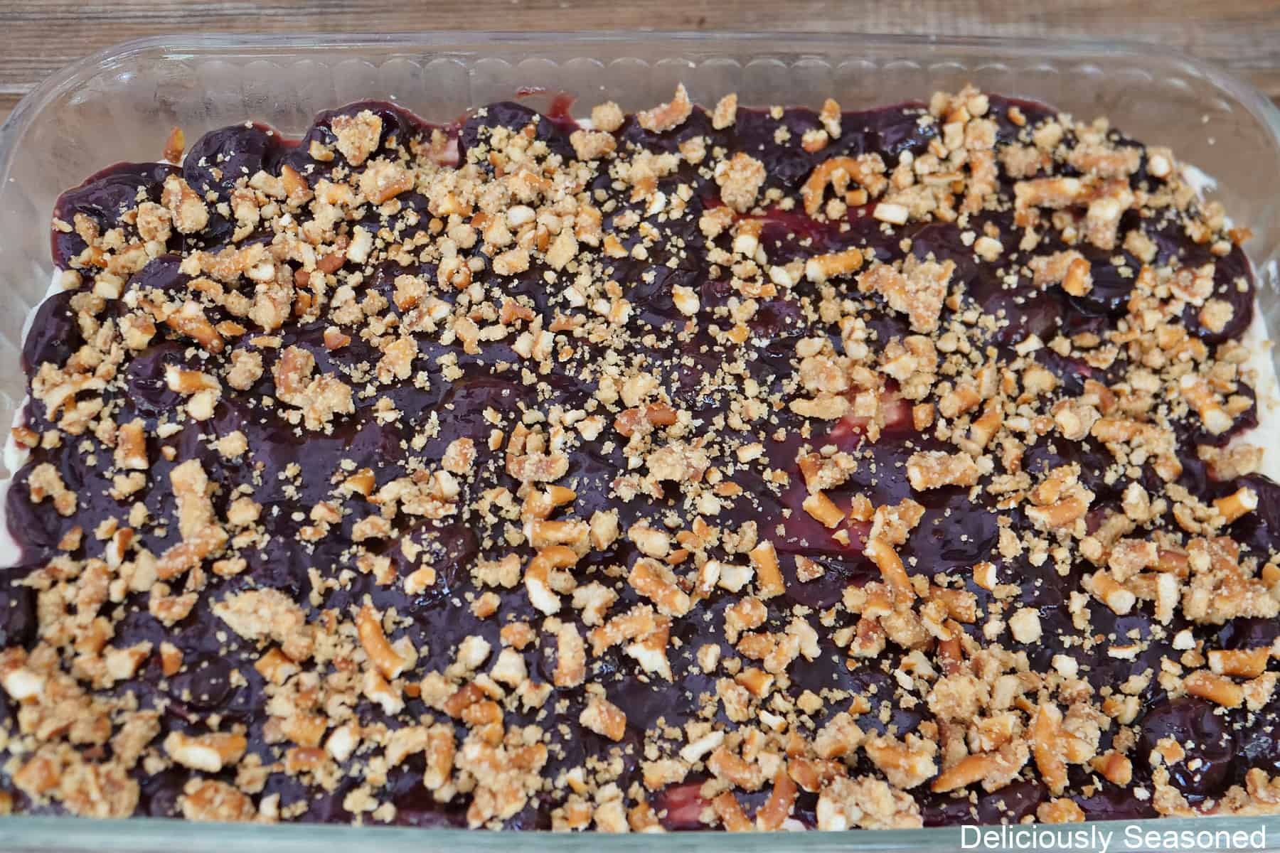 A 9 by 13 glass baking dish with the cherry pretzel salad in it after being layered, and topped with crushed pretzels.