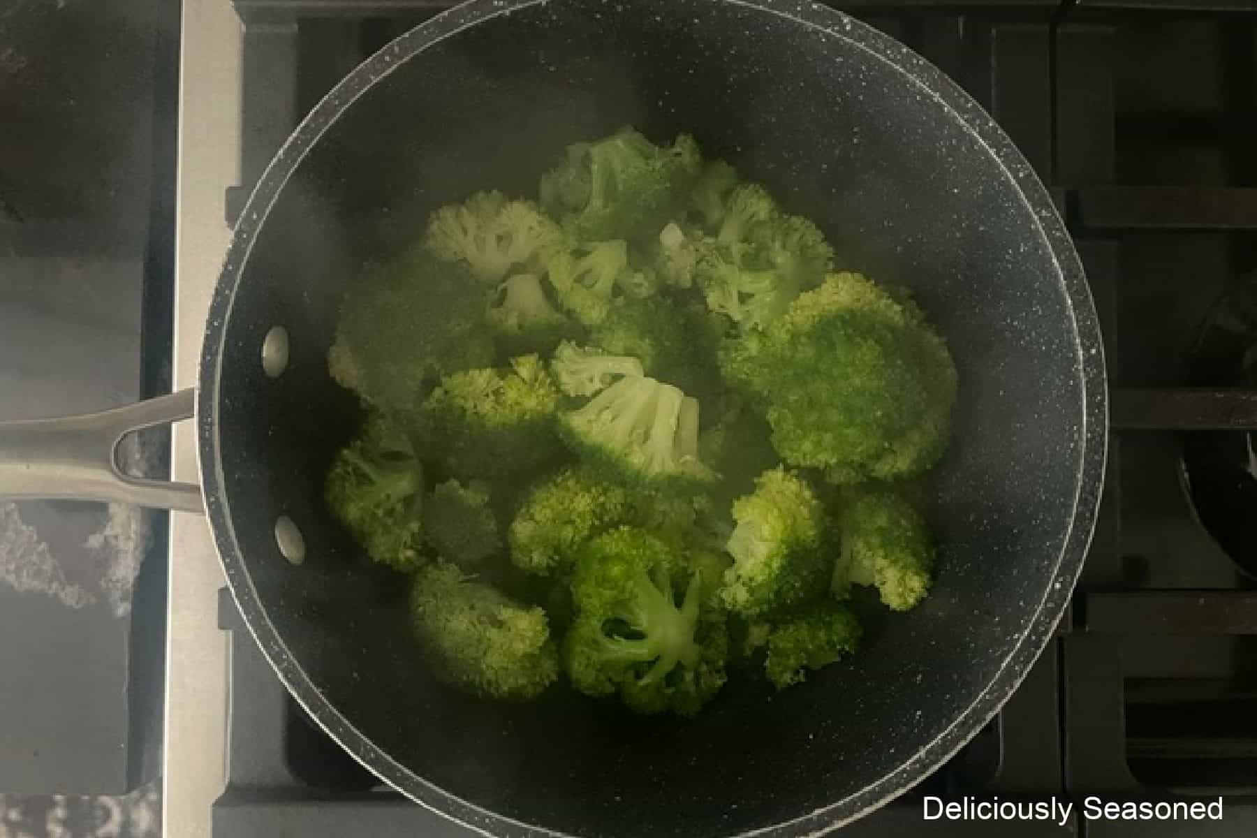 A saucepan on the stove with broccoli florets steaming in it.