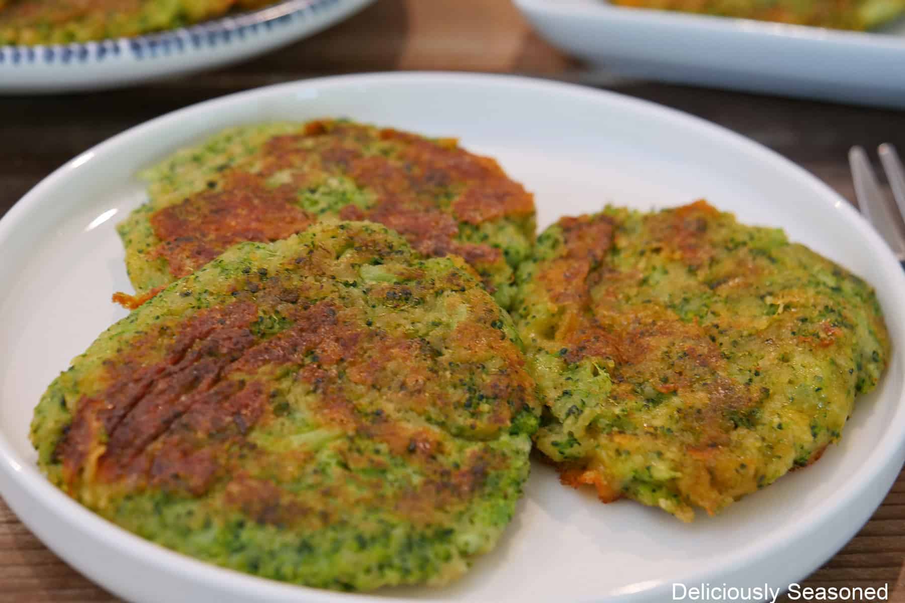 A round white plate with blue trim with three fried broccoli cheddar patties on it.