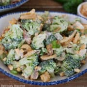 A white bowl with blue trim filled with a serving of loaded broccoli salad.
