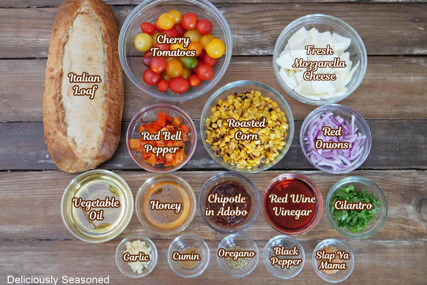 A wood surface with all the ingredients placed on it to make roasted corn panzanella salad.