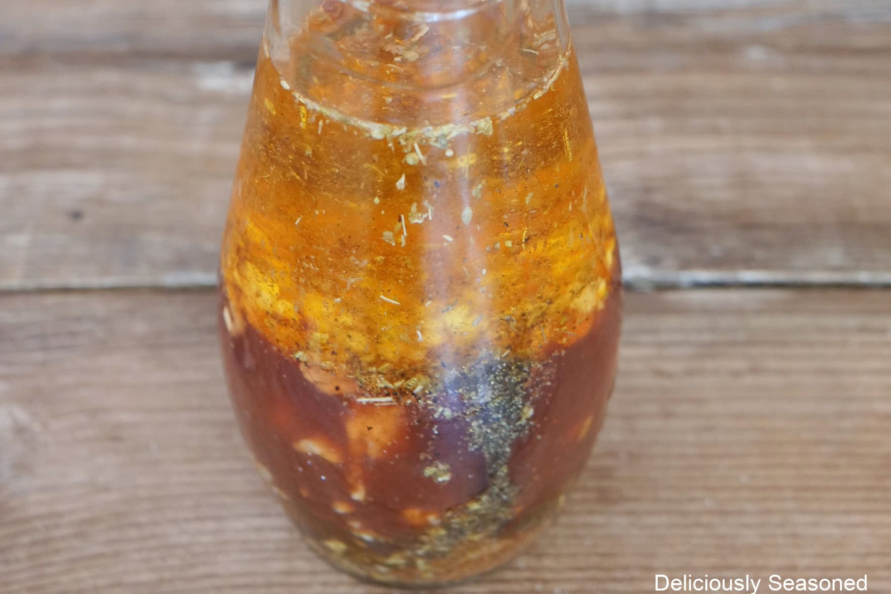 A wood surface with a bottle filled with honey chipotle dressing in it before being shaken and combined together.