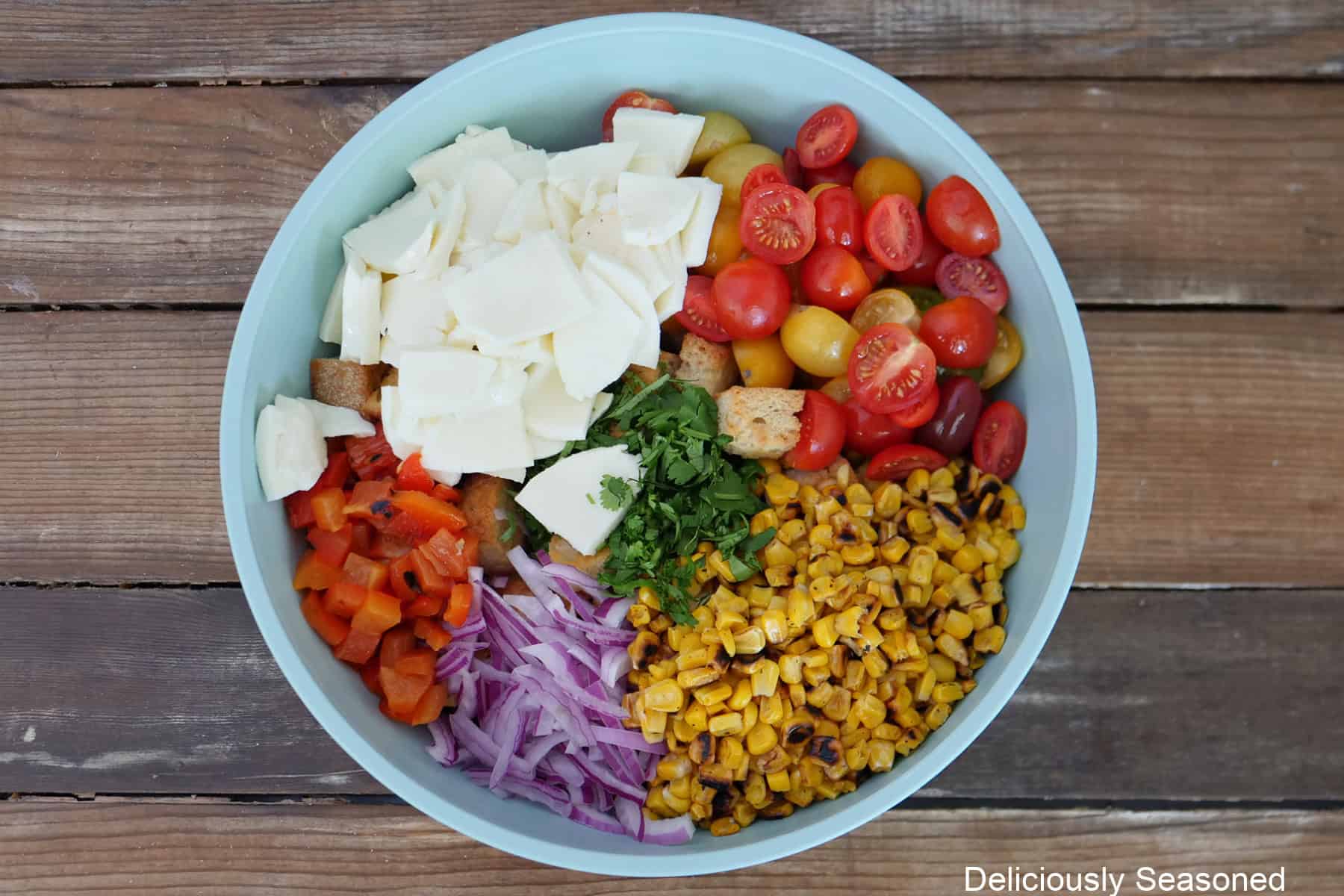 A large light blue bowl filled with all the ingredients for roasted corn panzanella salad before being stirred together.