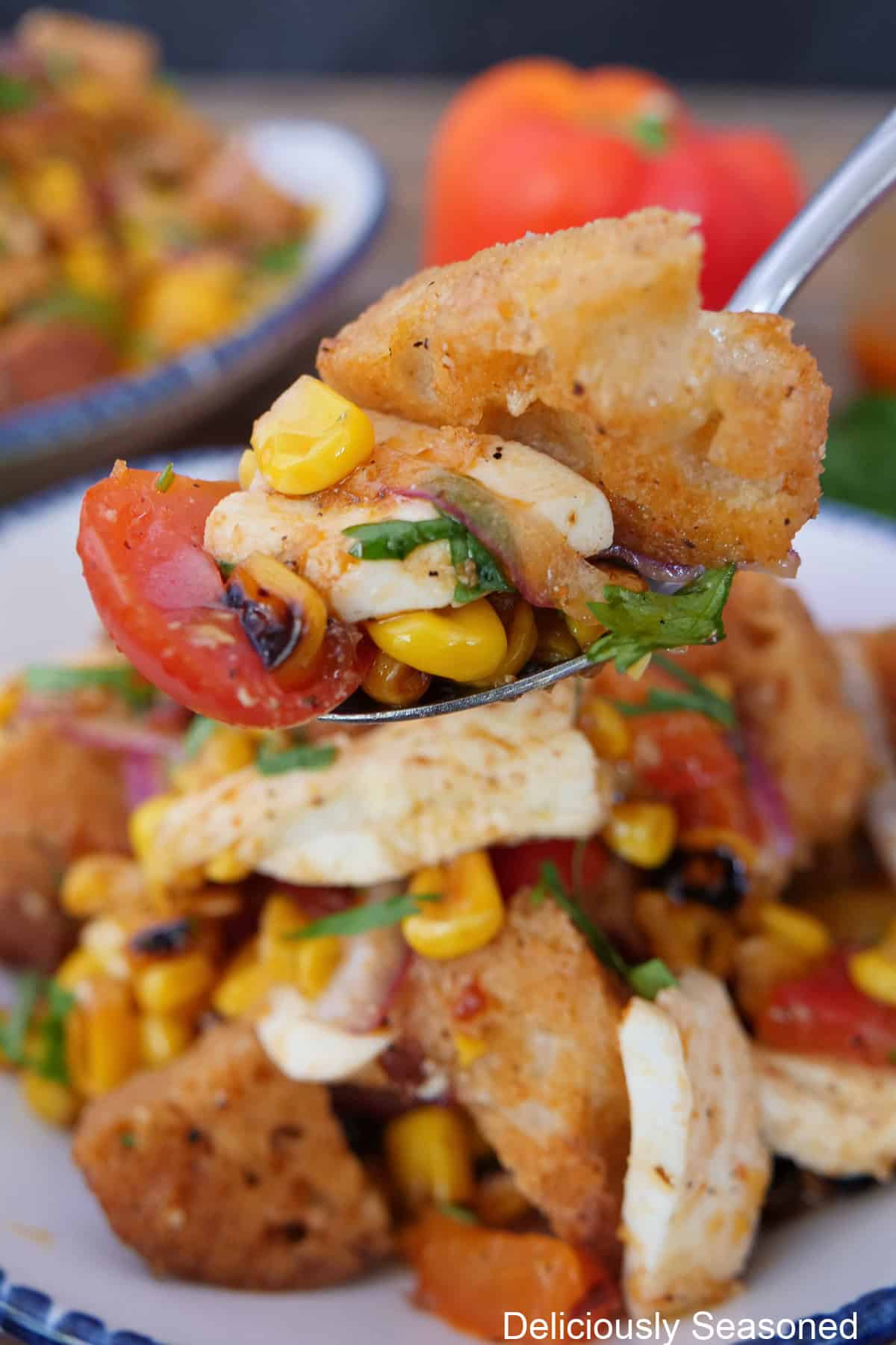 A bowl filled with roasted corn panzanella salad in it with a spoonful held above the bowl.