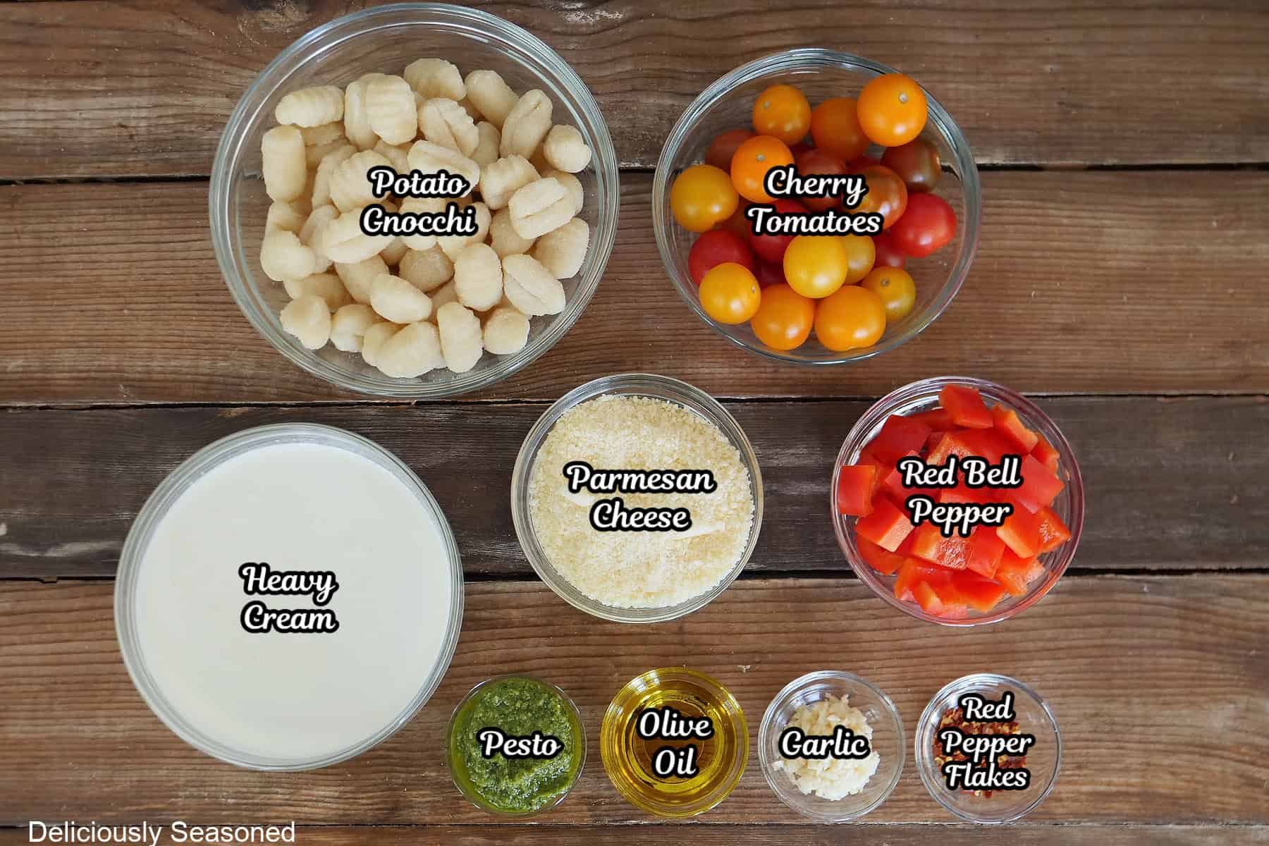 A wood surface with all the ingredients needed to make tomato pesto alfredo gnocchi placed on it.