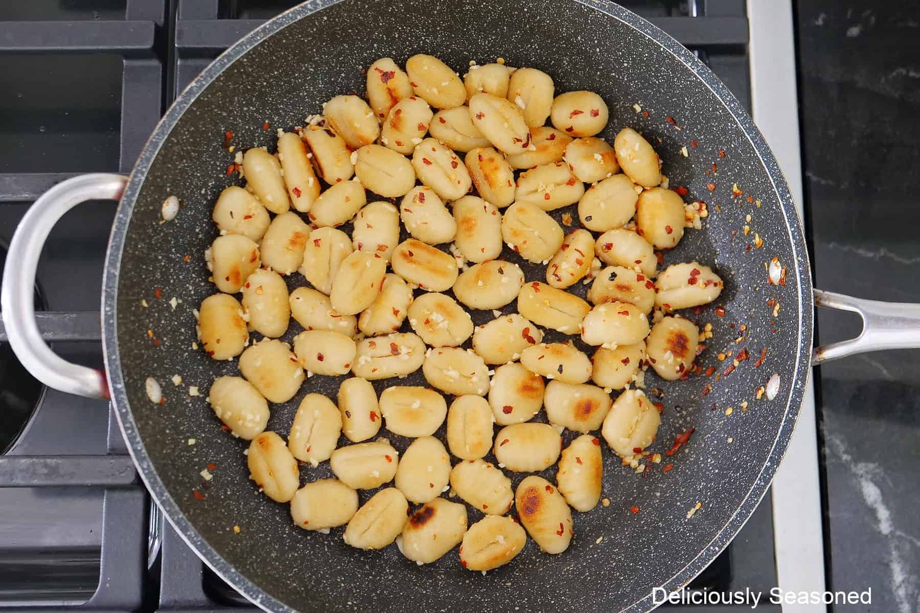A frying pan on the stove with gnocchi that has been fried with red pepper flakes and garlic stirred into it.