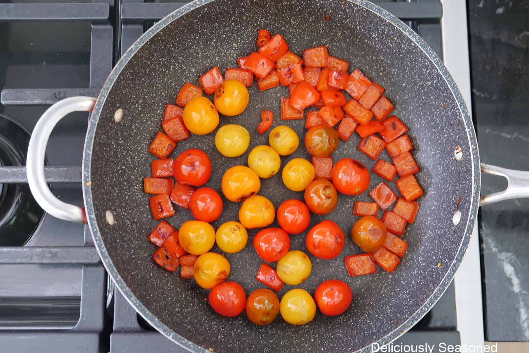 A frying pan on the stovetop with diced red bell pepper and cherry tomatoes in it.