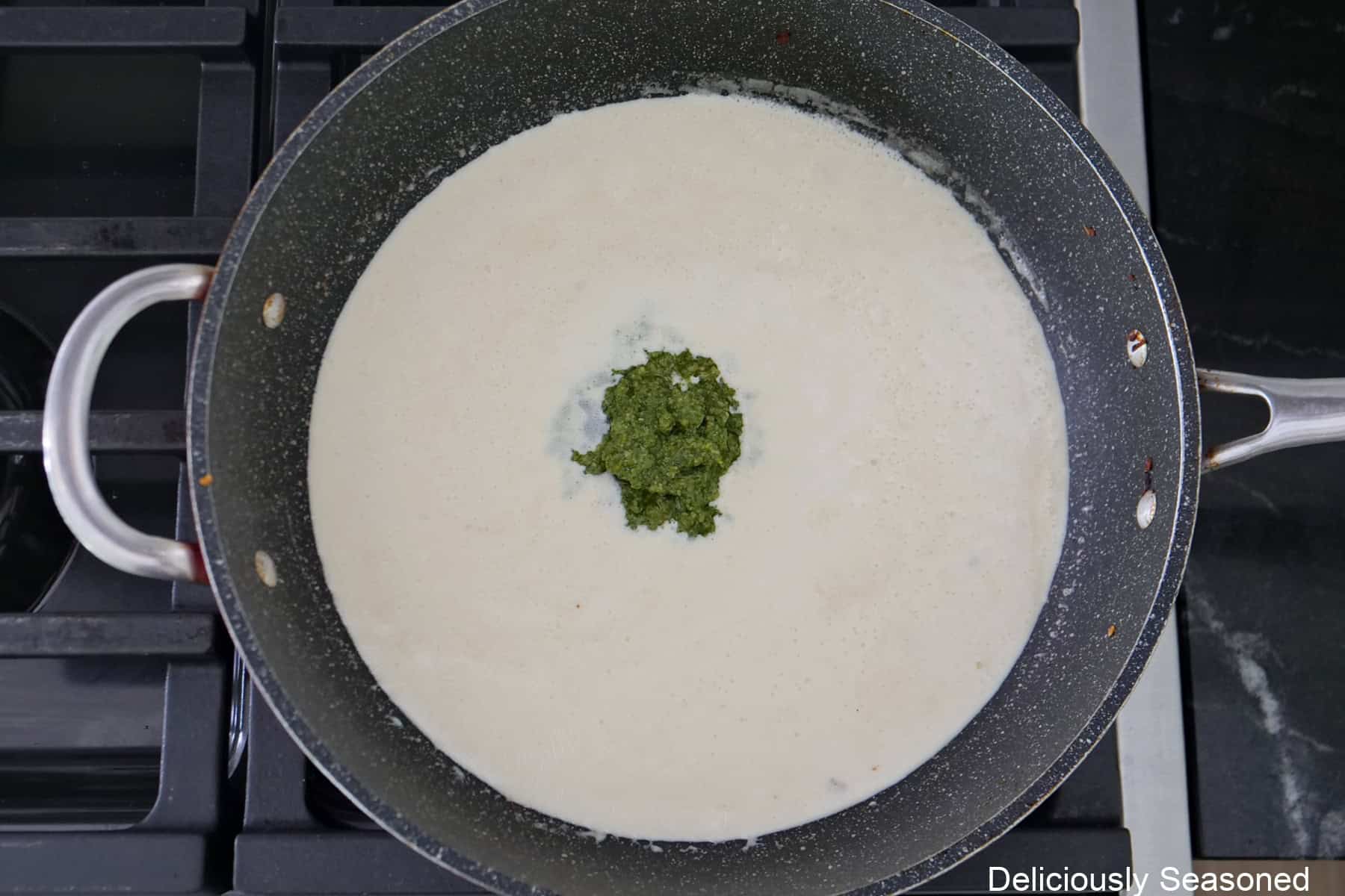 A frying pan with alfredo sauce in it with pesto being added.