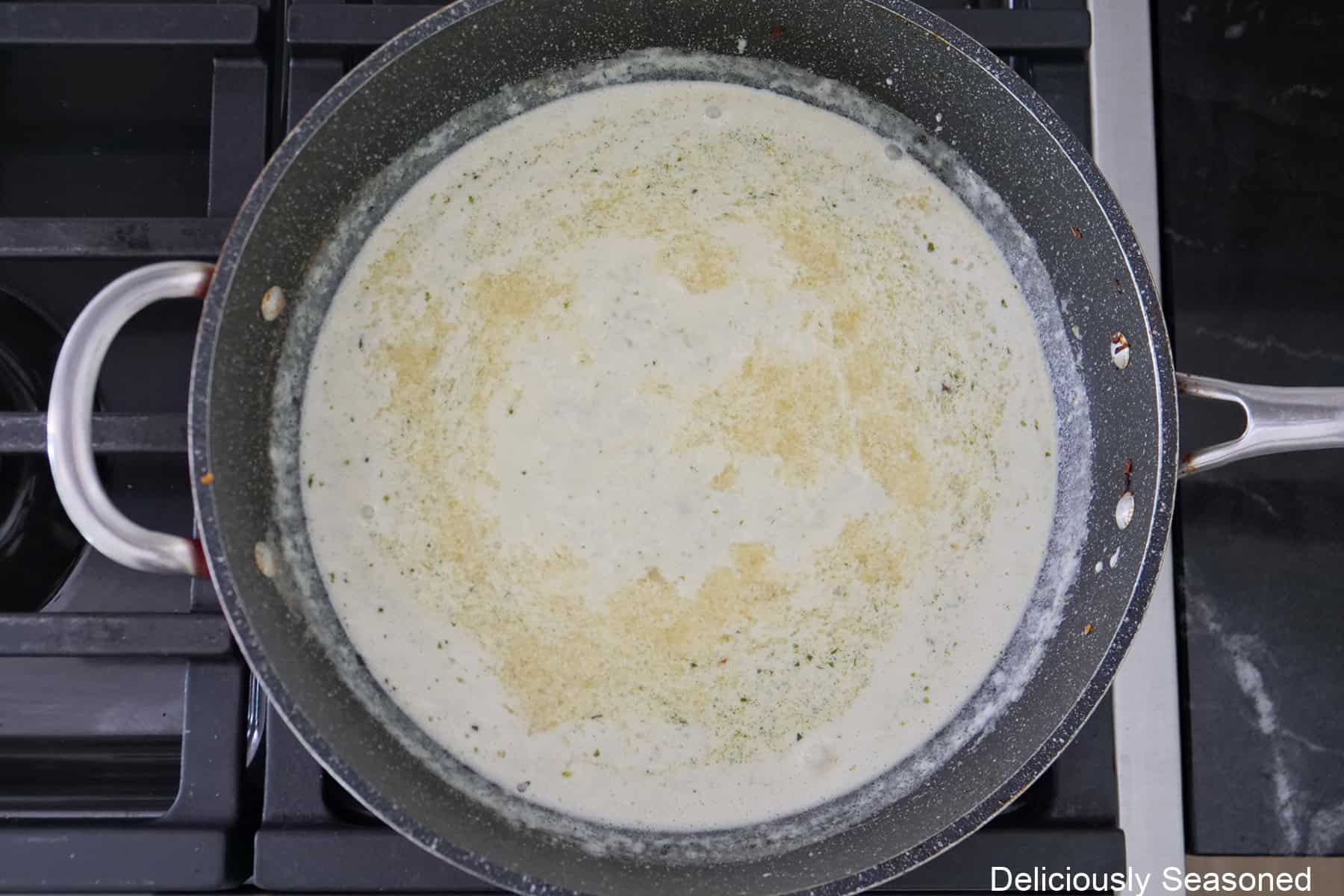 A frying pan on the stove with heavy cream and Parmesan cheese stirred together.