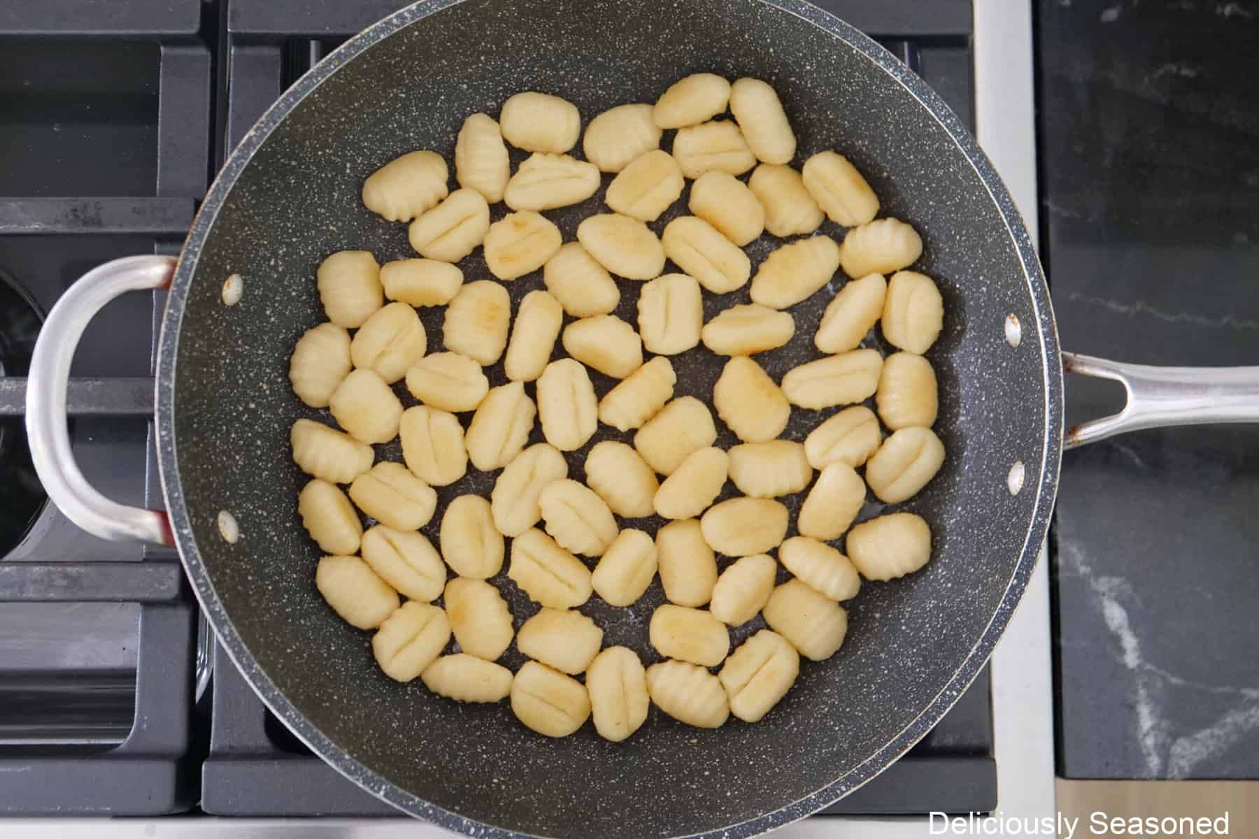 A frying pan on the stovetop with fried potato gnocchi.