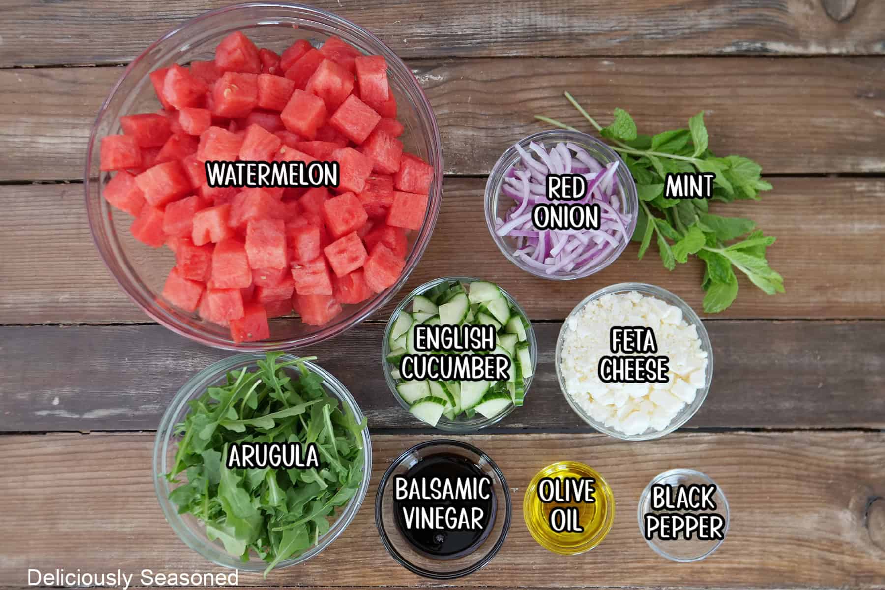 A rustic wood surface with all the ingredients placed on it to make watermelon feta salad.