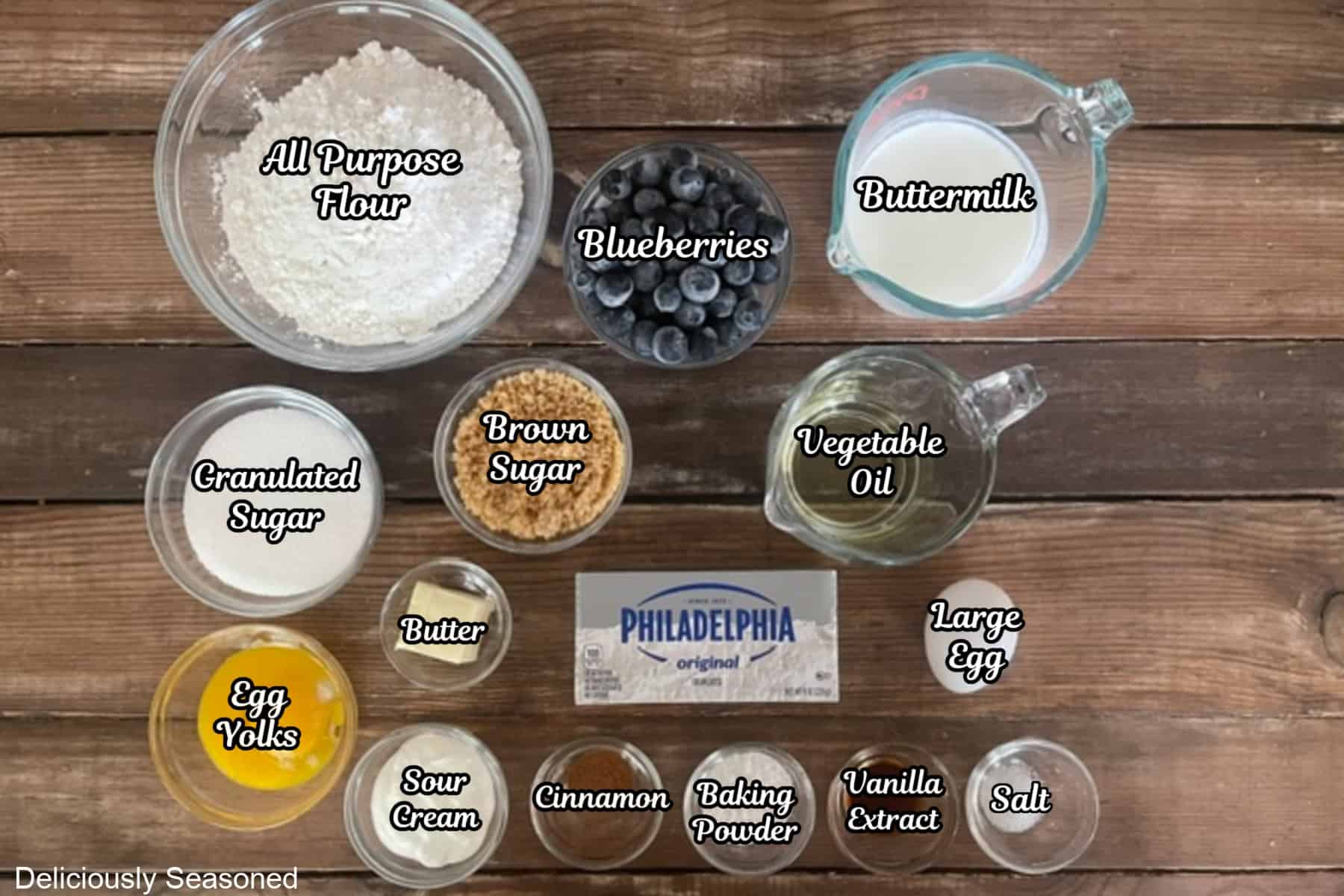 A wood surface with all the ingredients placed on it to make blueberry cream cheese muffins.