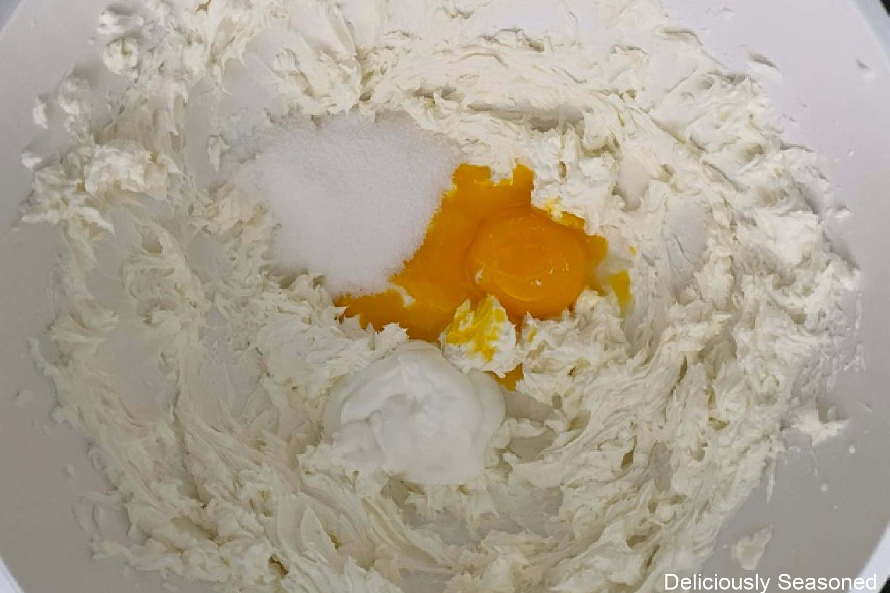 A white mixing bowl with cream cheese filling ingredients in it.
