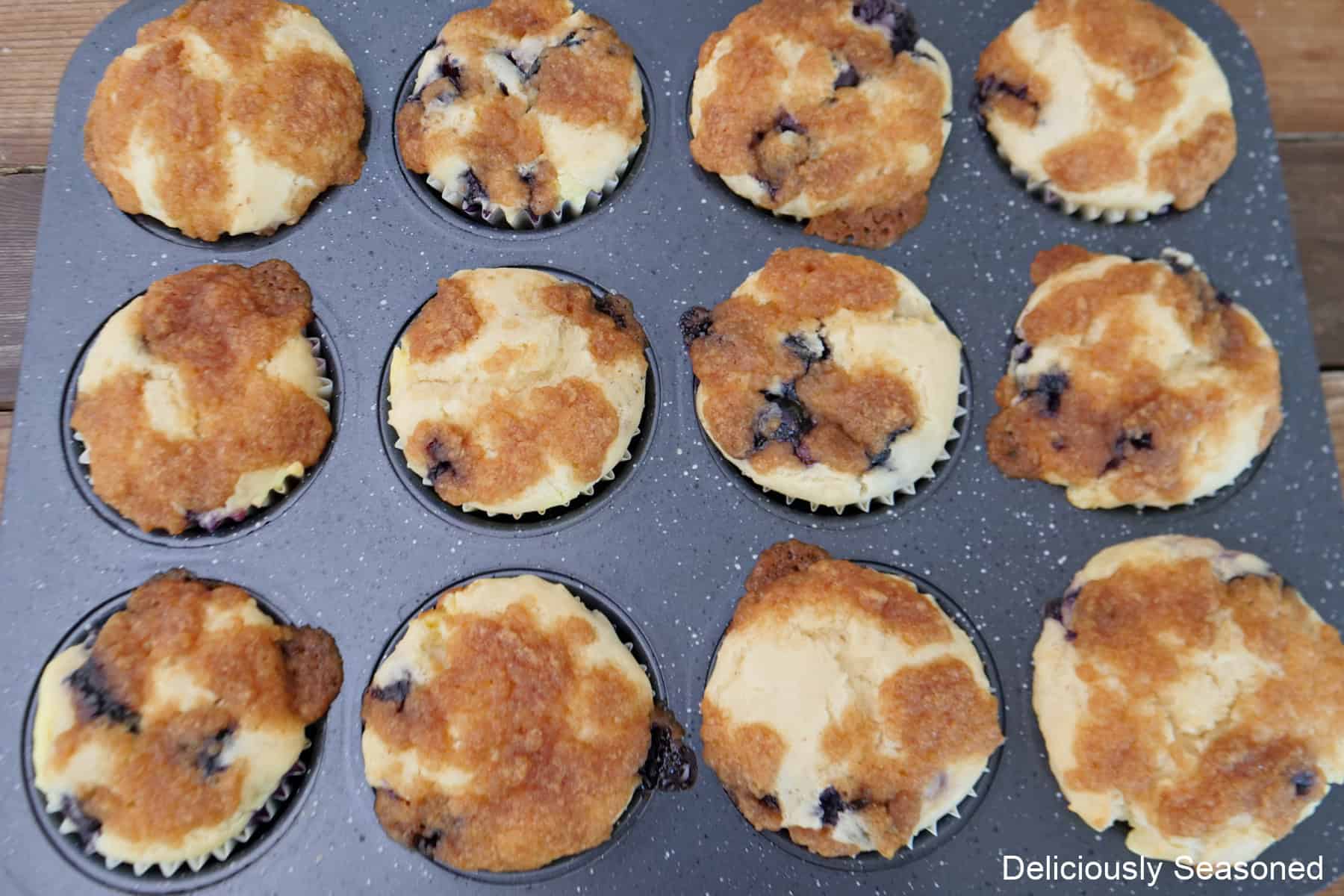 A 12-count muffin tin with baked blueberry cream cheese muffins in it.