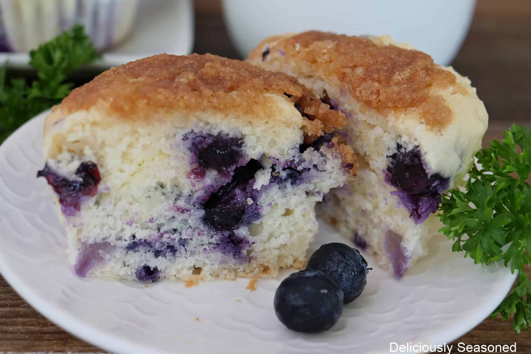 A white plate with a blueberry cream cheese muffin that is cut in half.