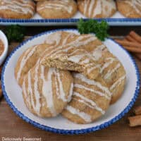 A wood surface with a blue trimmed white plate with five brown butter snickerdoodles on it with a bite taken out of the one on top.