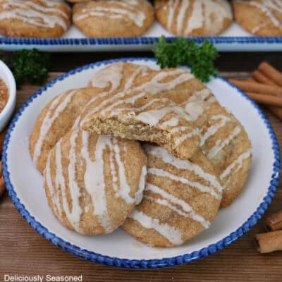 A wood surface with a blue trimmed white plate with five brown butter snickerdoodles on it with a bite taken out of the one on top.