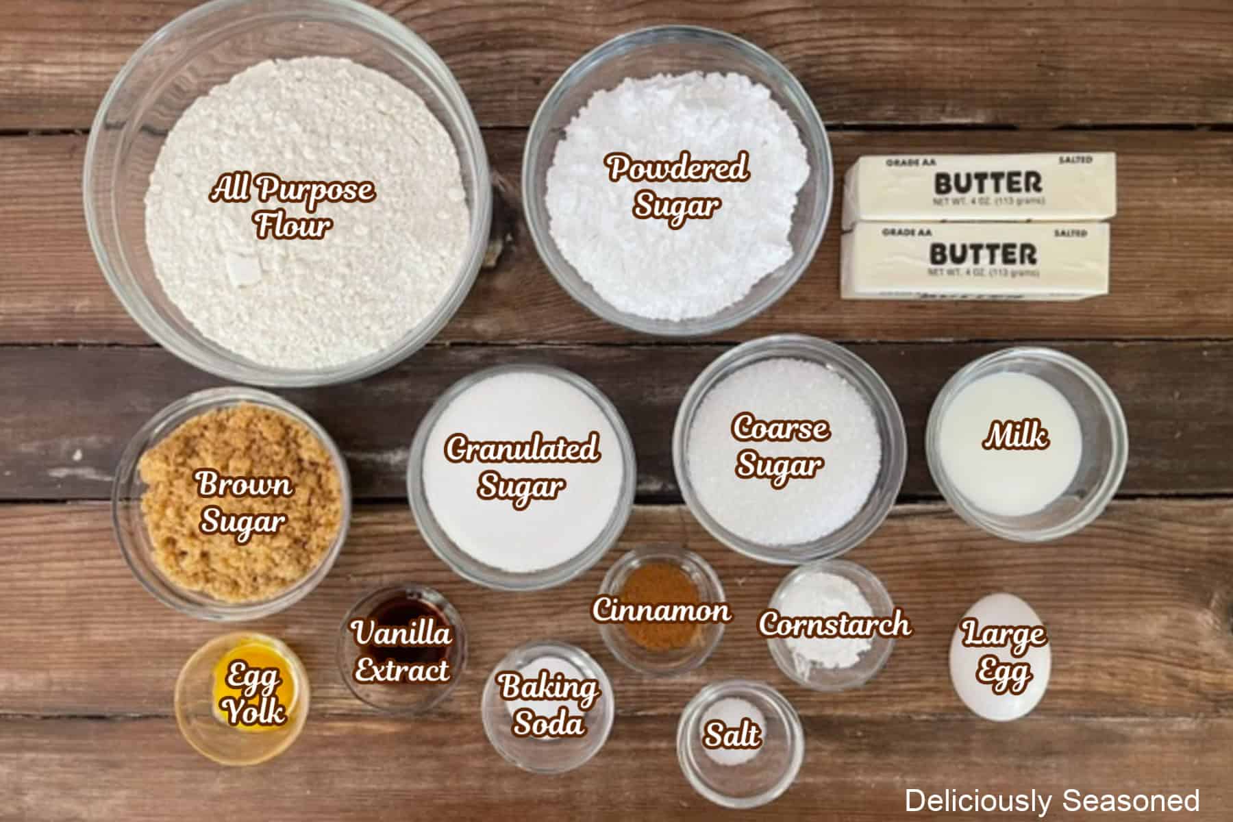 A wood surface with all the ingredients placed on it to make brown butter snickerdoodle cookies.