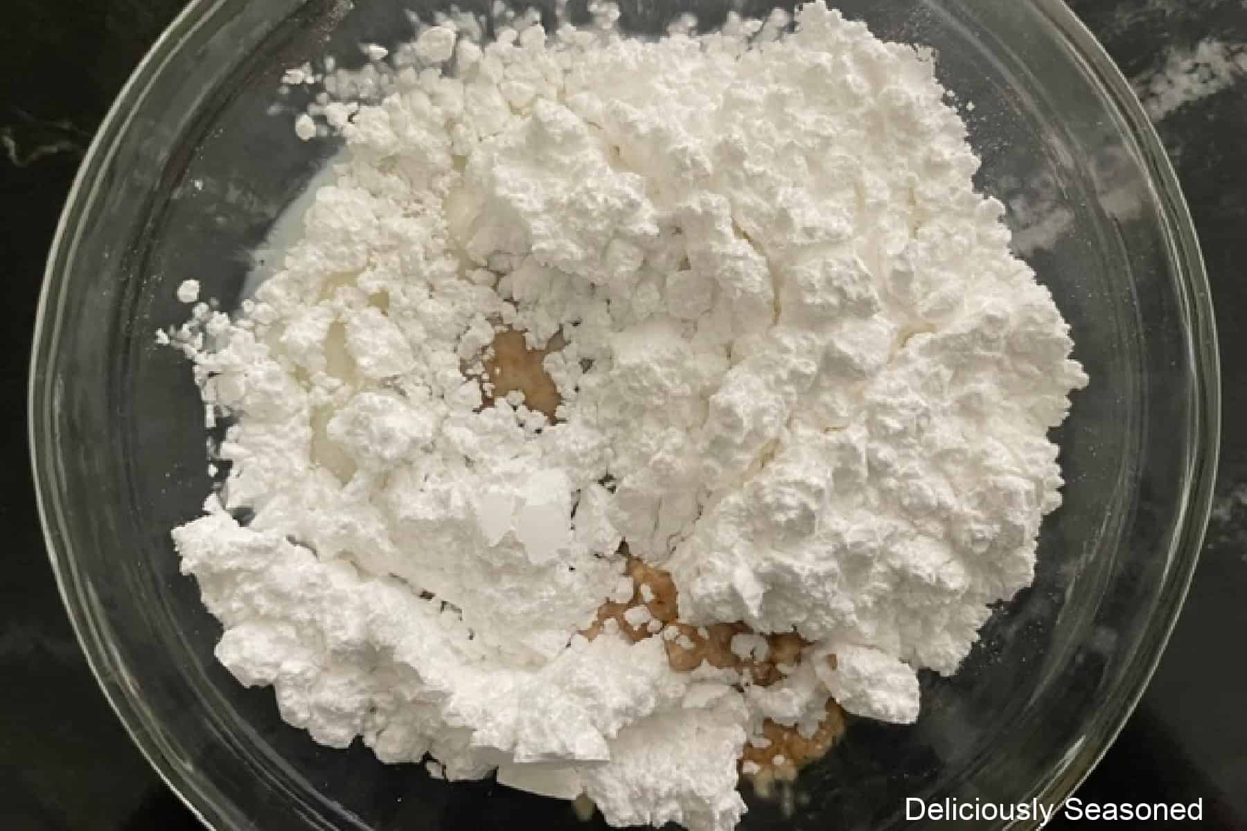 A glass bowl filled with powdered sugar, milk, and vanilla in it before being mixed together.