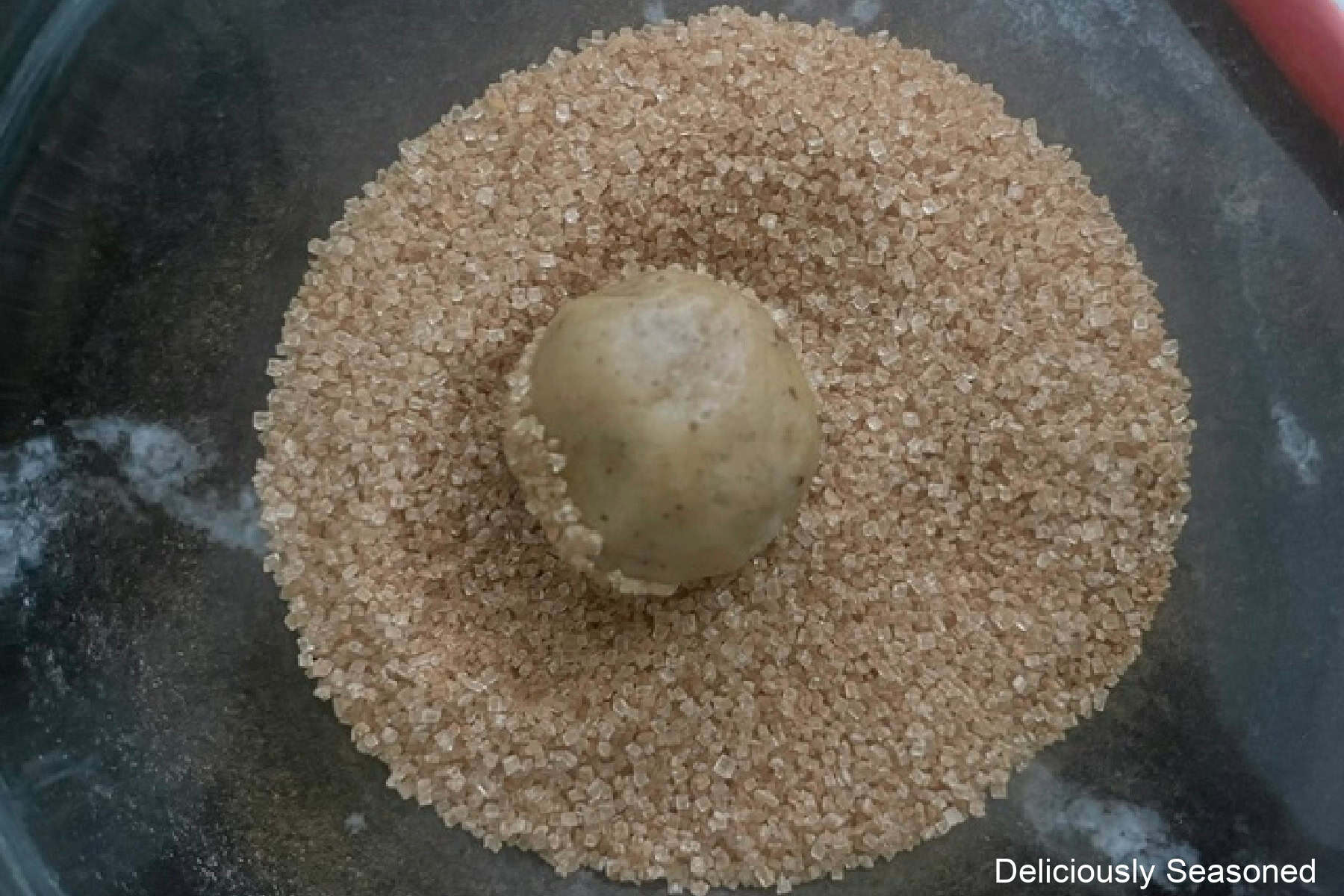 A bowl filled with cinnamon and sugar and a snickerdoodle dough ball rolled in the cinnamon sugar mixture.
