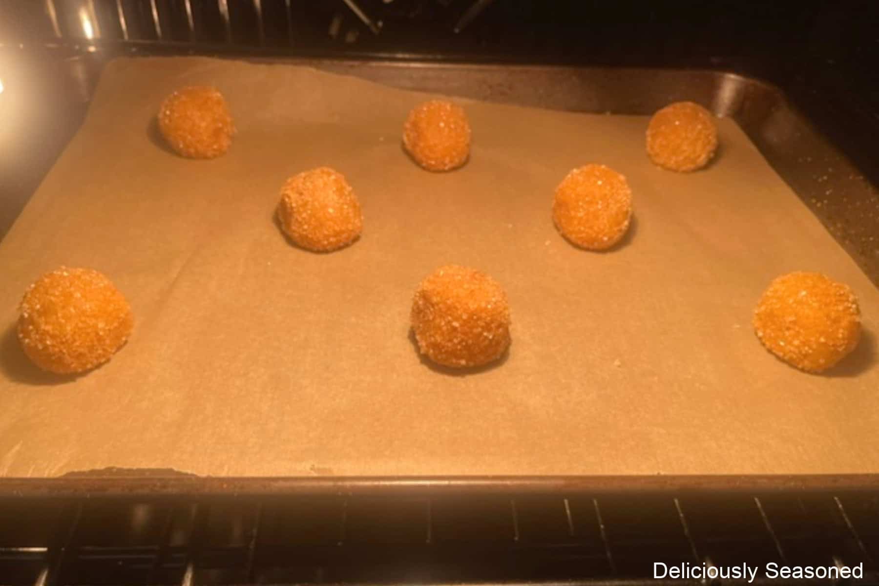 A baking sheet in the oven with eight snickerdoodle dough balls on it.