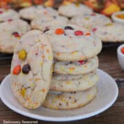 A white plate with blue trim with a stack of fall sugar cookies on it with more cookies in the background.
