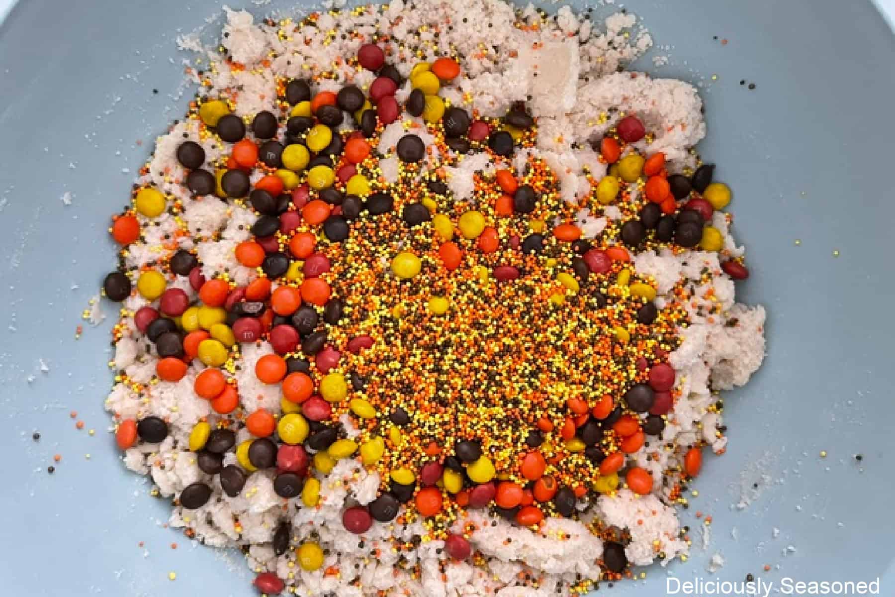 Sugar cookie batter with mini M&Ms and fall candy sprinkles added before being combined together.