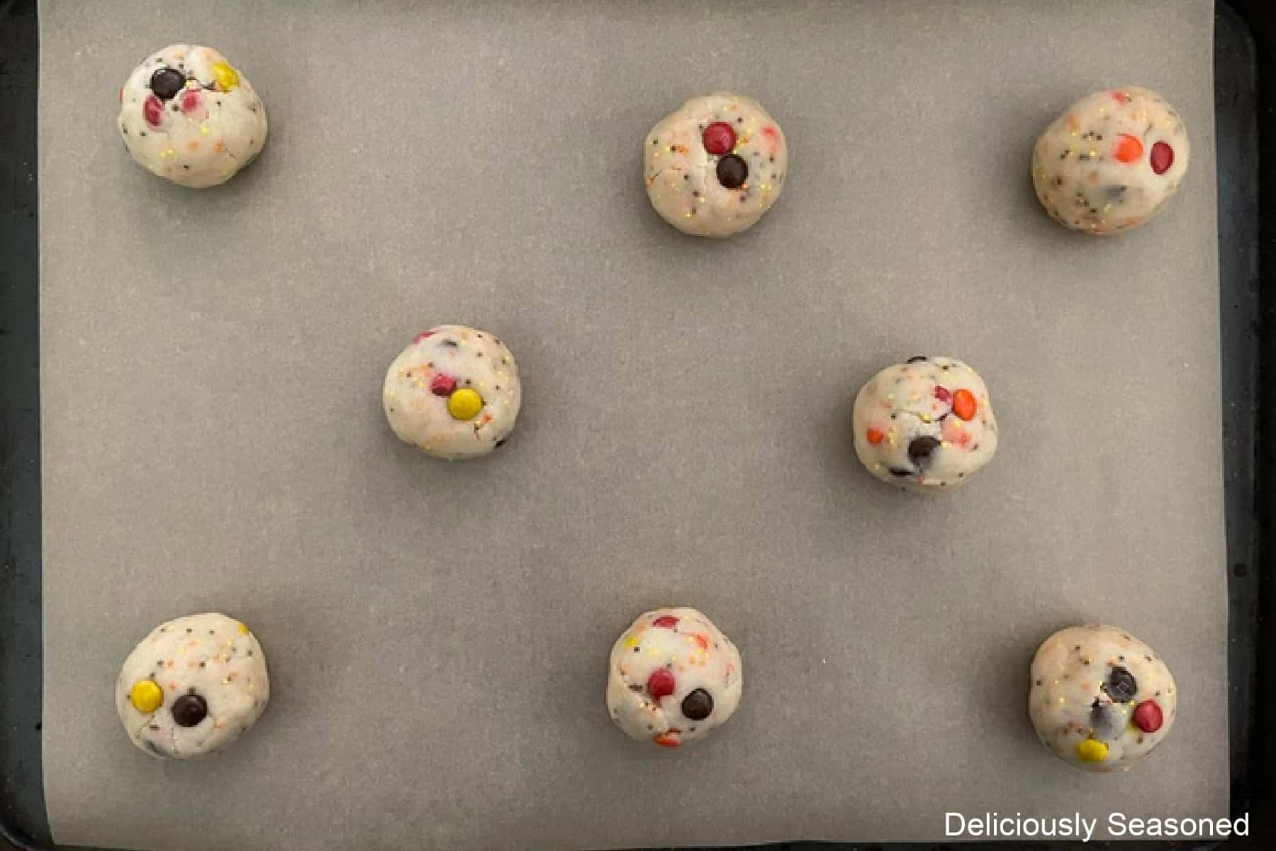 A parchment lined baking sheet with eight sugar cookie dough balls on it.