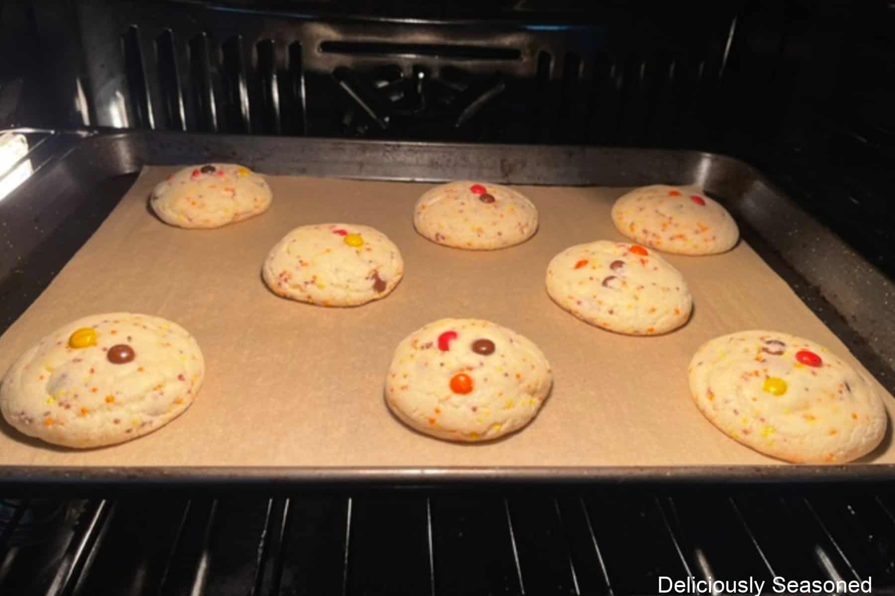 A baking sheet in the oven with eight sugar cookies baking on it.