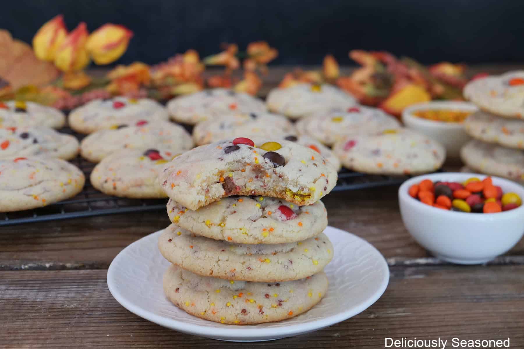 A wood surface with fall sugar cookies placed on it with a small bowl for mini M&Ms next to the cookies.