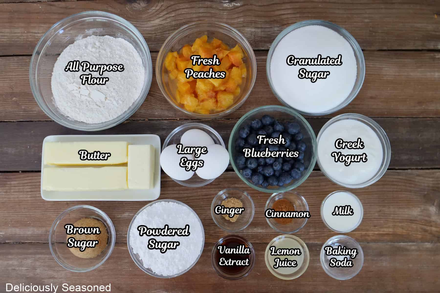 A wood surface with all the ingredients placed on it to make peach blueberry bundt cake.