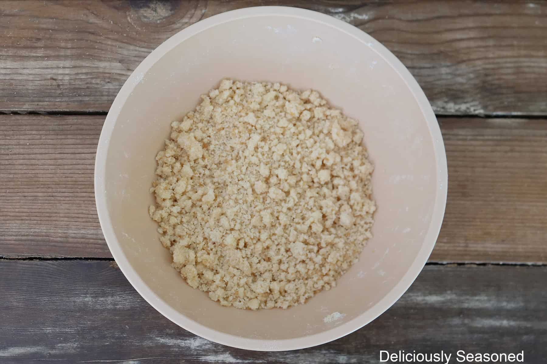 A wood surface with a white mixing bowl filled with streusel ingredients in it.
