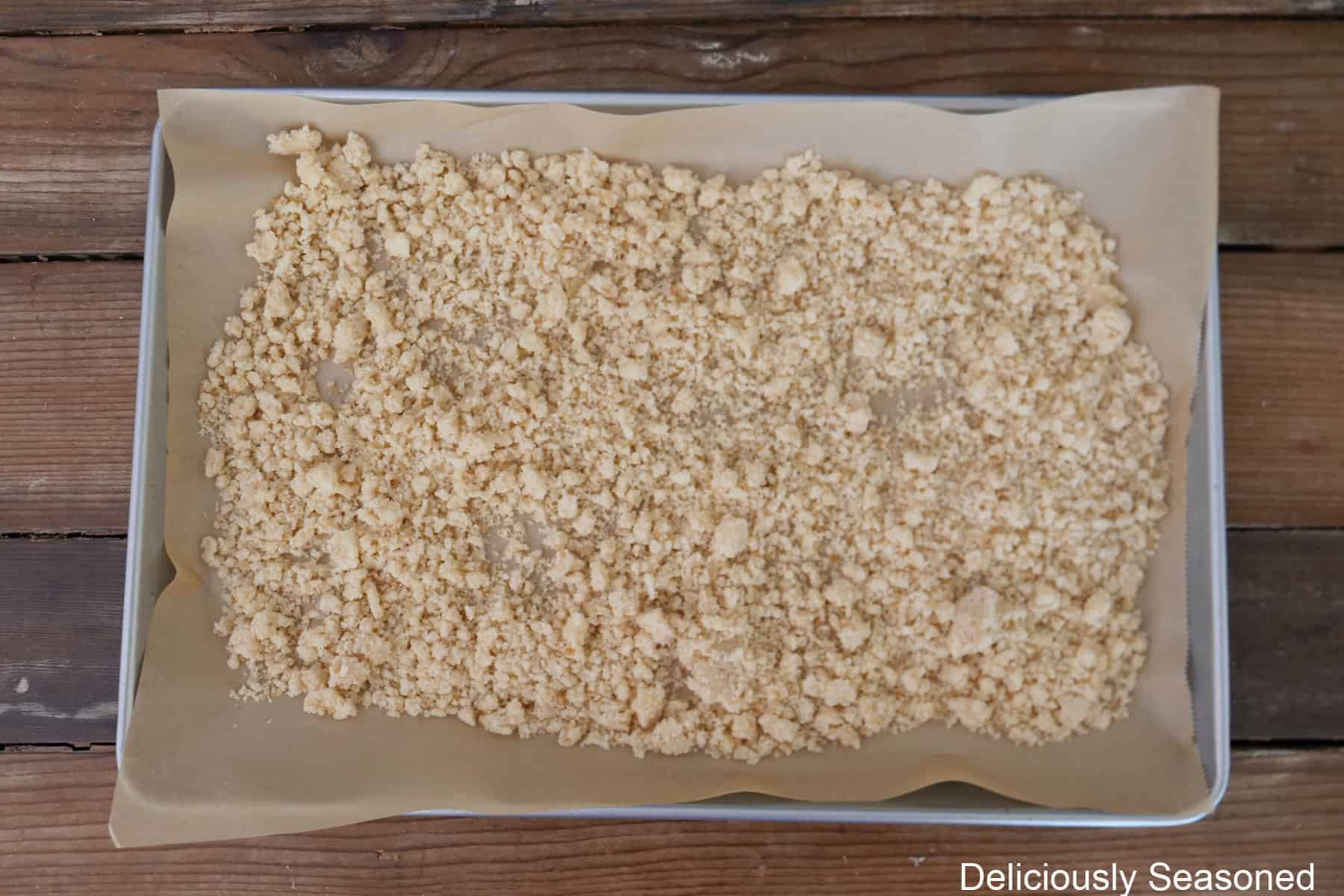 A baking sheet lined with parchment paper and streusel spread out in an even layer.