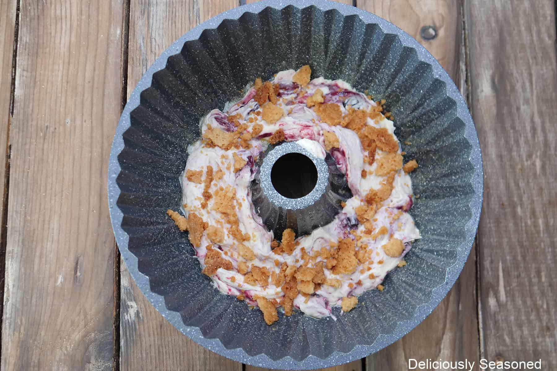 A wood surface with a bundt pan placed on it with the first layer of batter and topped with streusel.