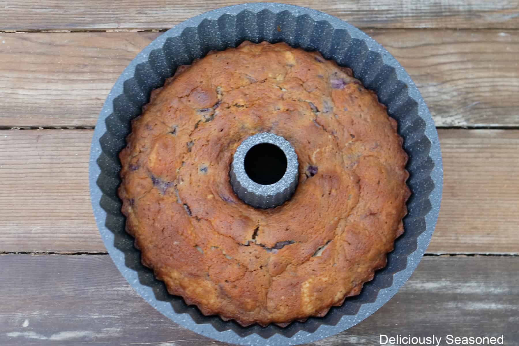 A wood surface with a peach blueberry Bundt cake still in the bundt pan after being baked.