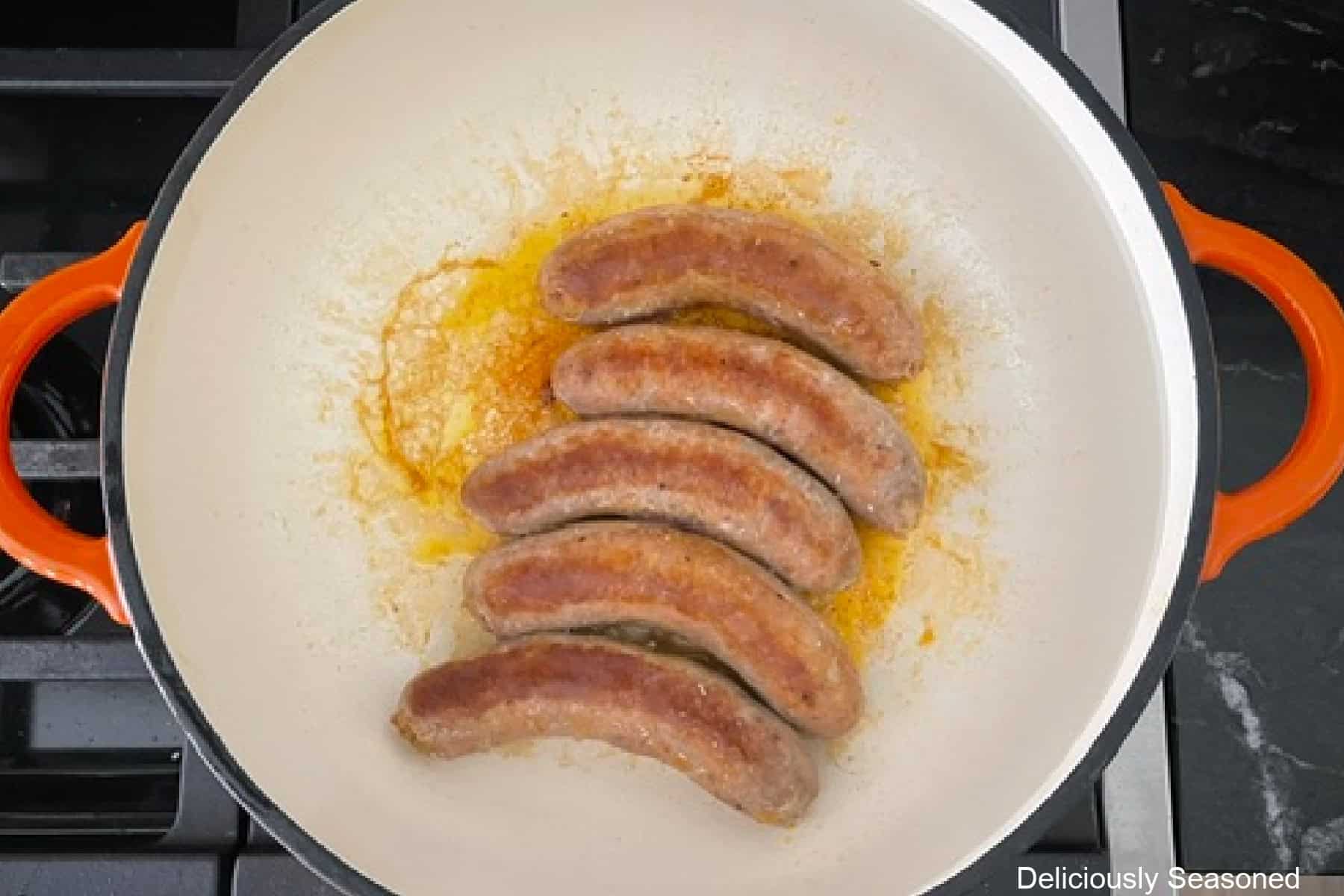 A frying pan with five Italian sausage links cooking in it.