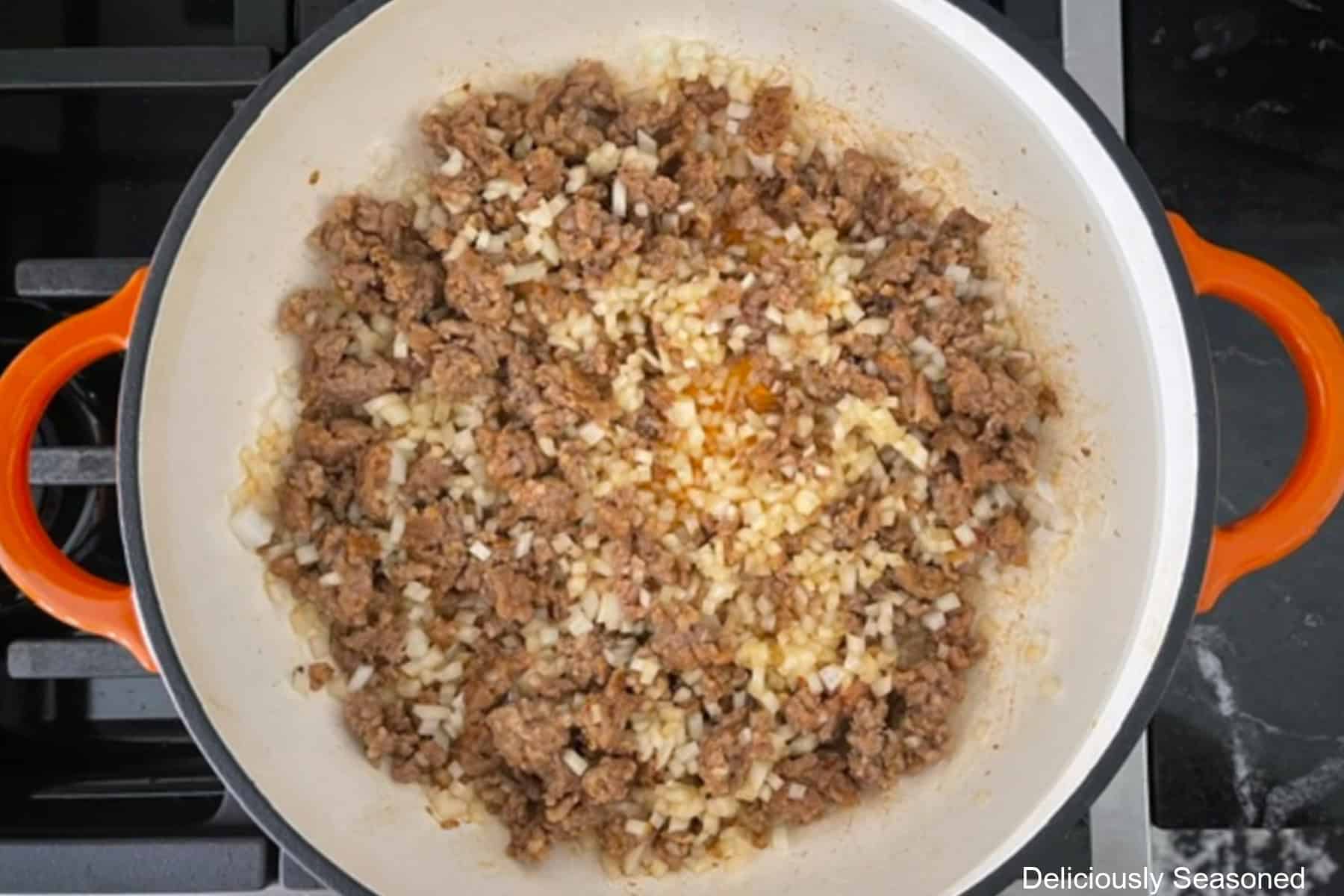 A frying pan with ground Italian sausage and diced onions cooking in it.