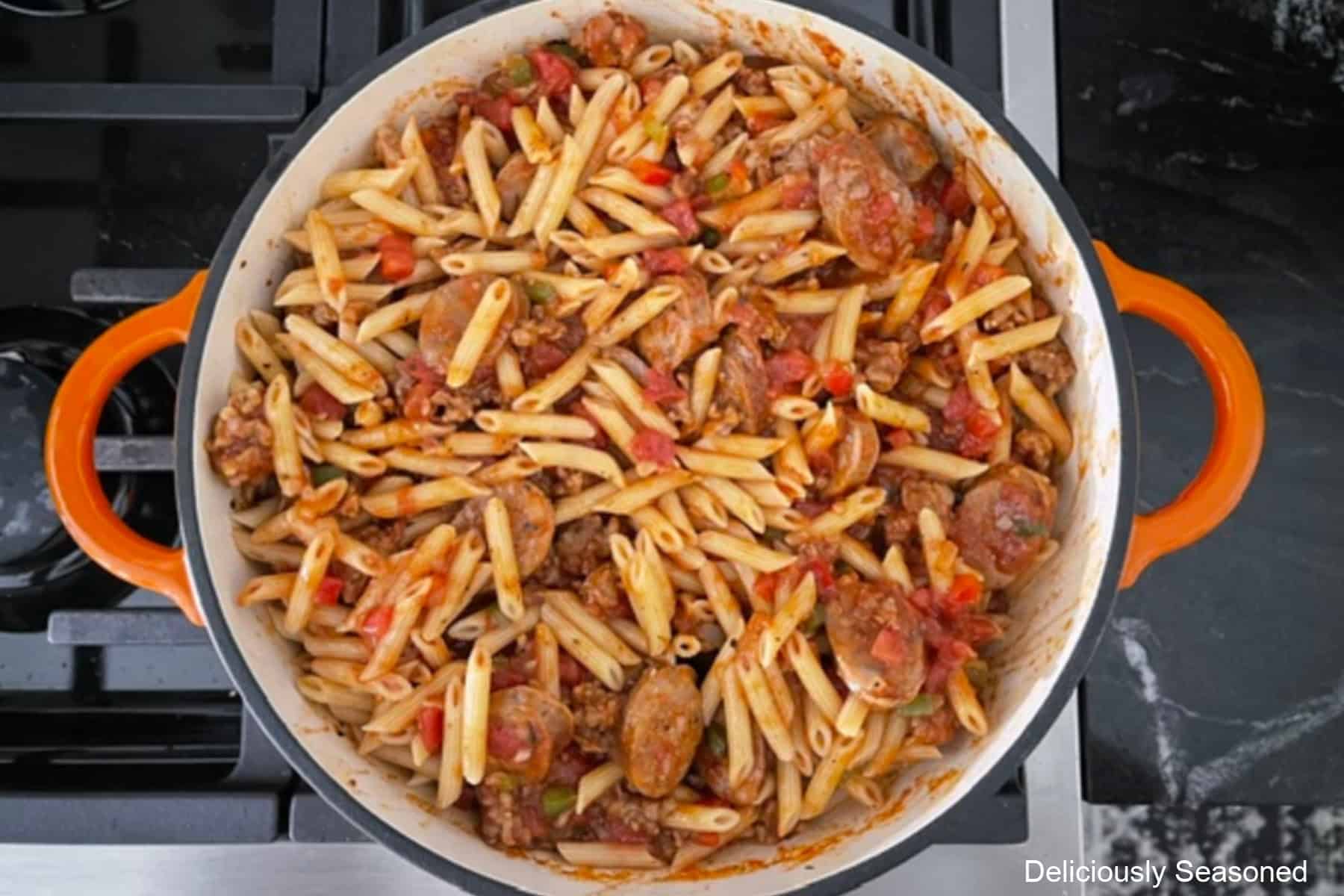 A frying pan with the Italian sausage sauce with penne pasta added.