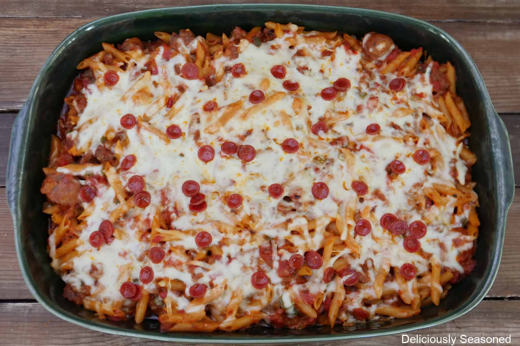 A 9 by 13 green baking dish with a baked pepperoni sausage pizza pasta in it.